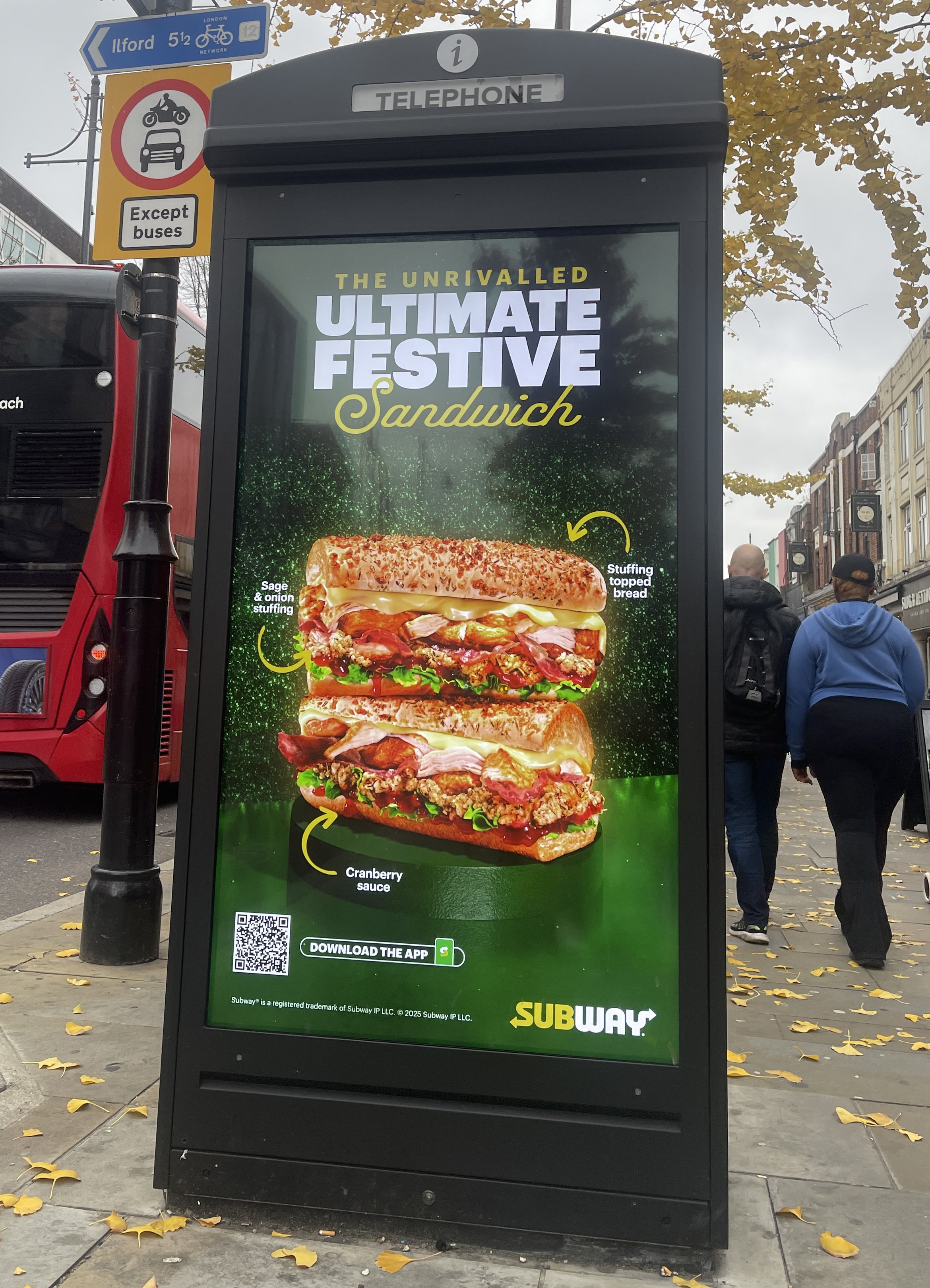 A digital billboard advertising the 'Ultimate Festive Sandwich' from Subway, featuring a large sandwich with sage and onion stuffing, cranberry sauce, and various meats, set against a green background with yellow accents and text.