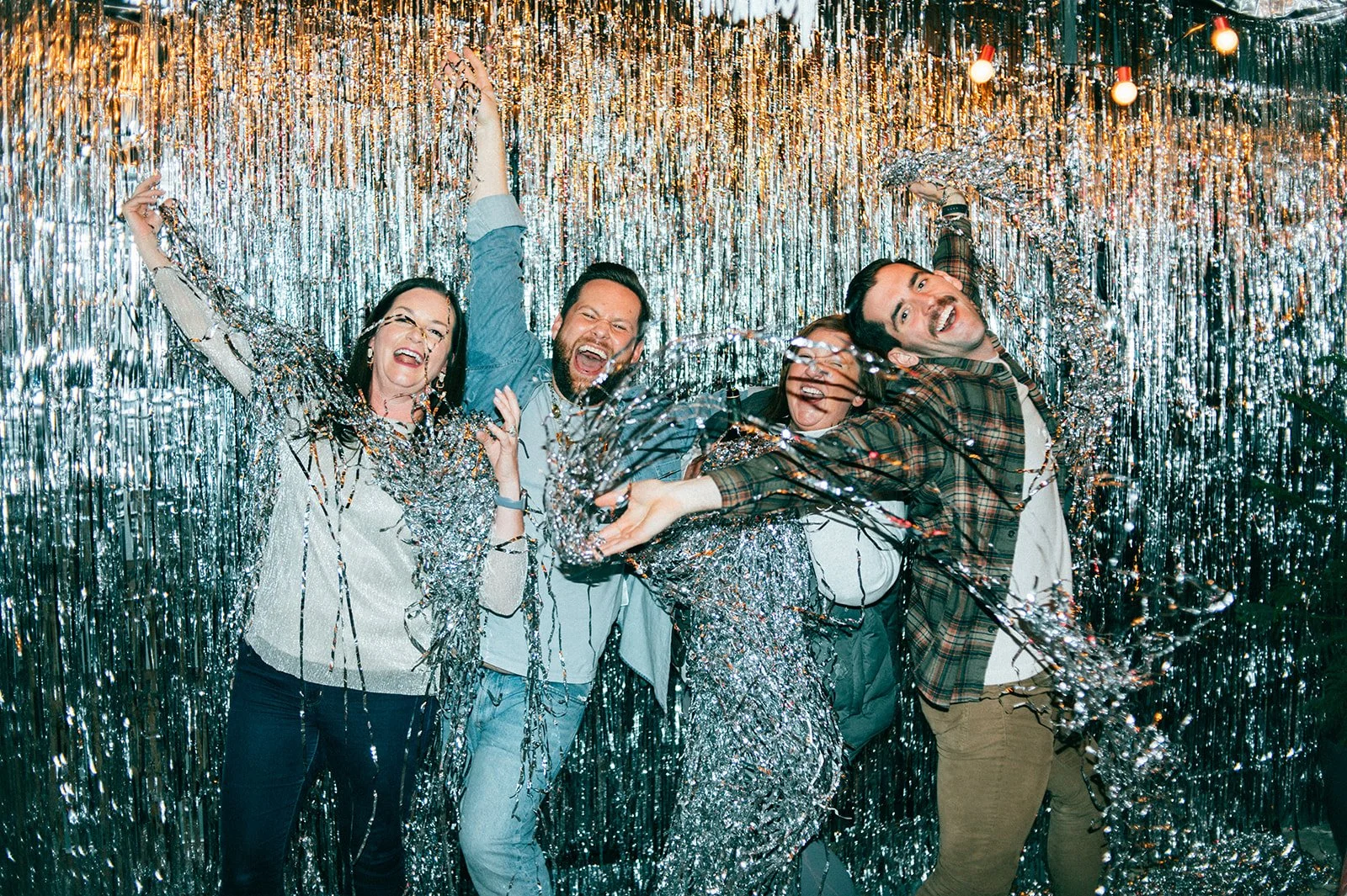 Group of five people celebrating with festive silver streamers and gold tinsel backdrop.