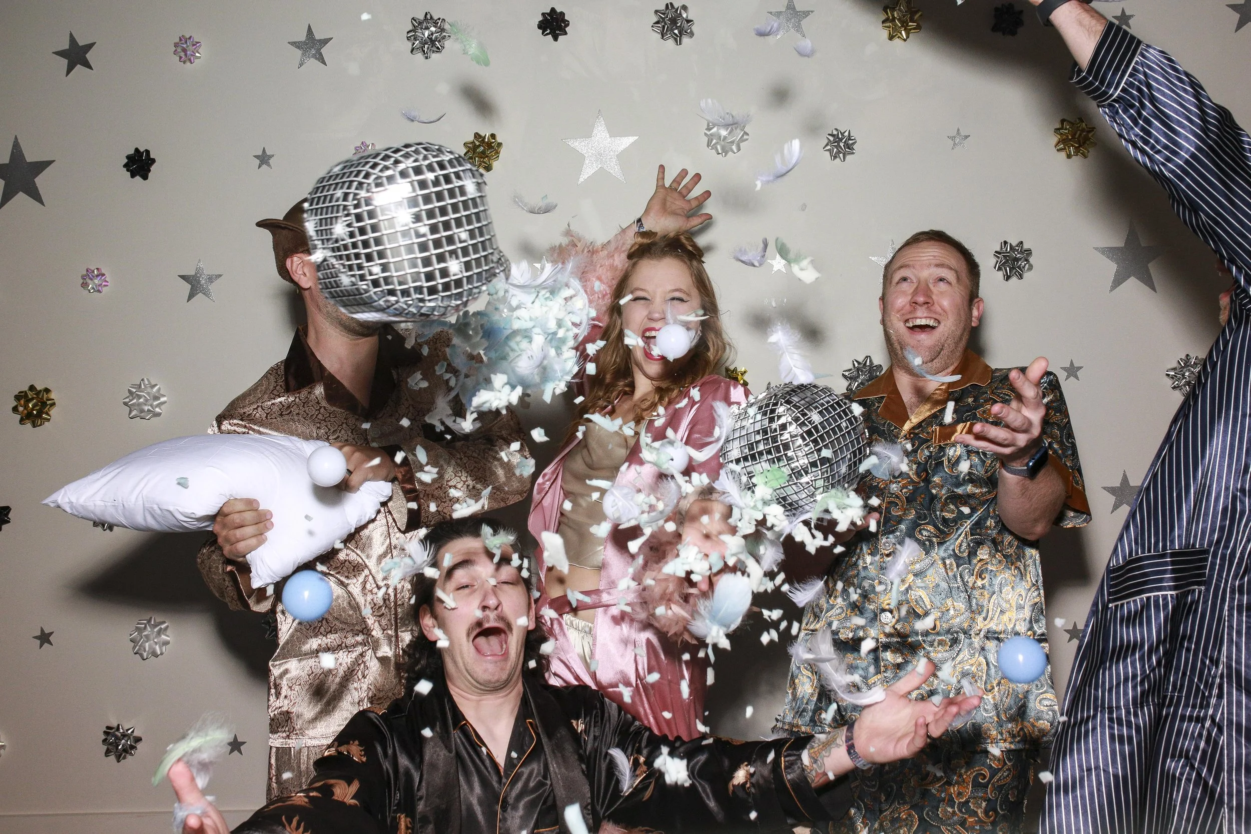 Group of people celebrating with confetti, star and bow decorations on the wall, and disco balls.