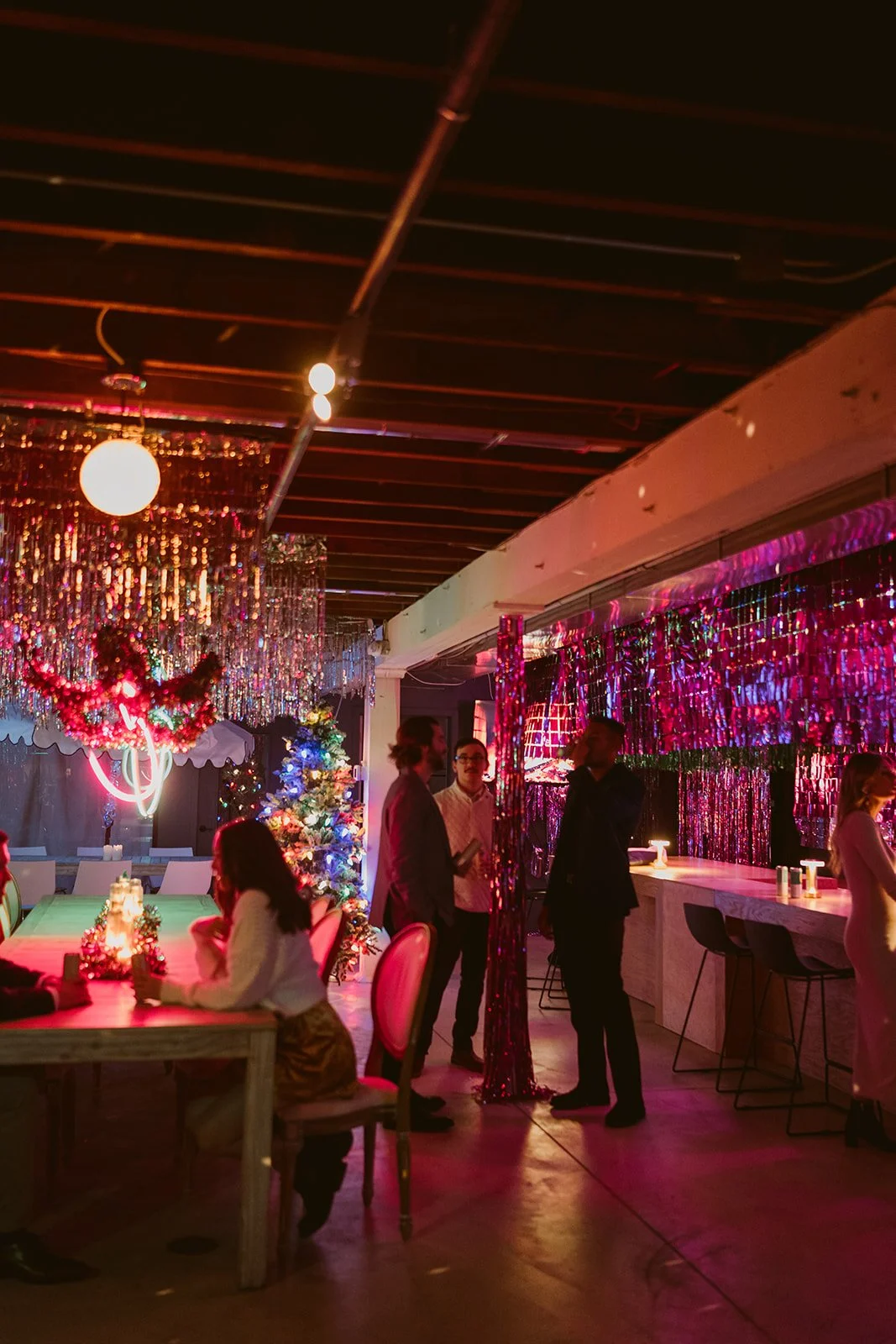 People socializing at a Christmas-themed party with decorations, a Christmas tree, and festive lights.