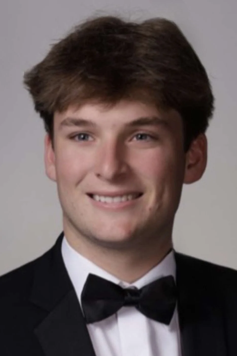 Young man in a suit and tie smiling against a blue background.