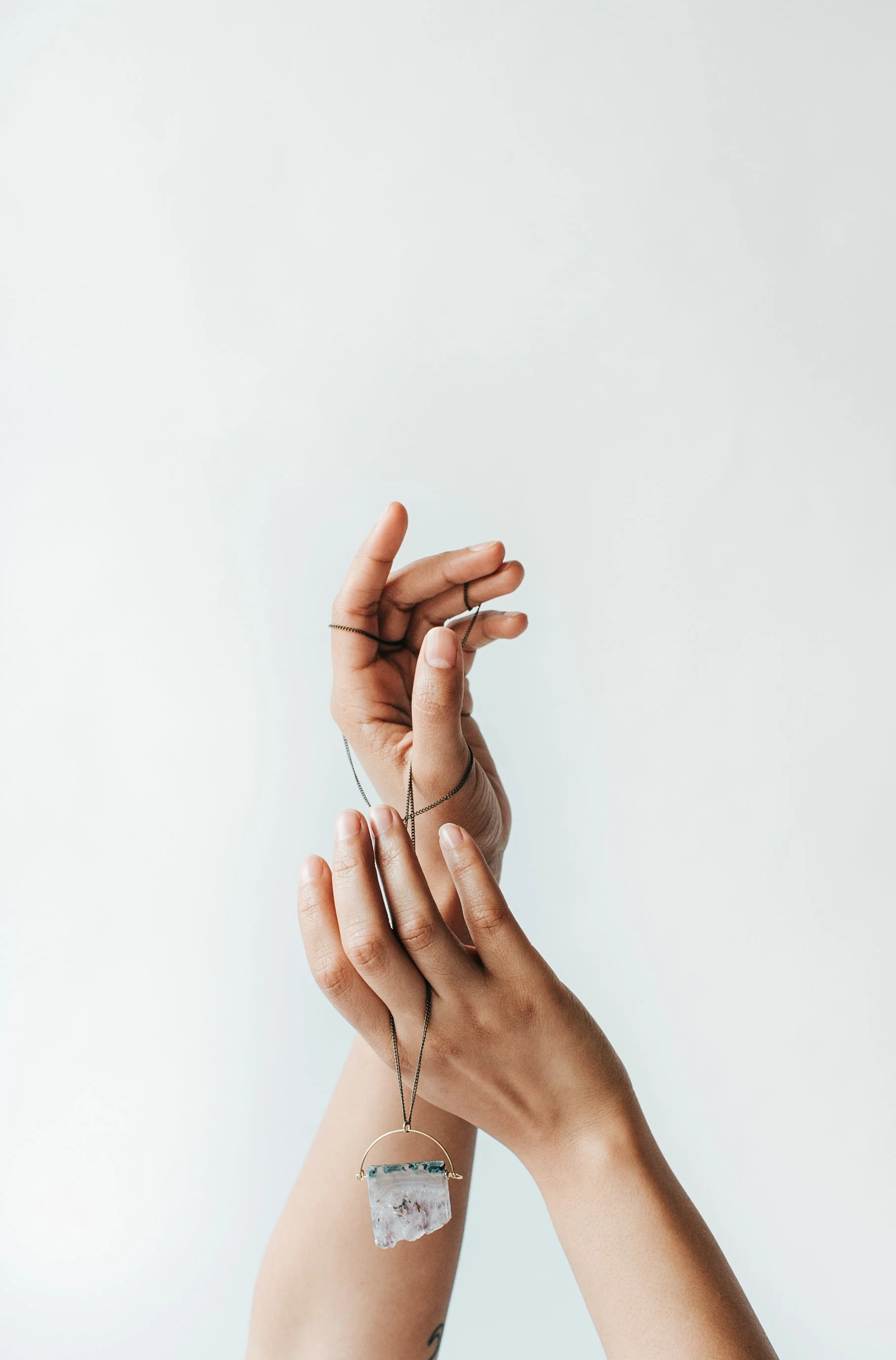 Close-up of hands holding a necklace with a large, irregularly shaped crystal pendant against a plain light background.