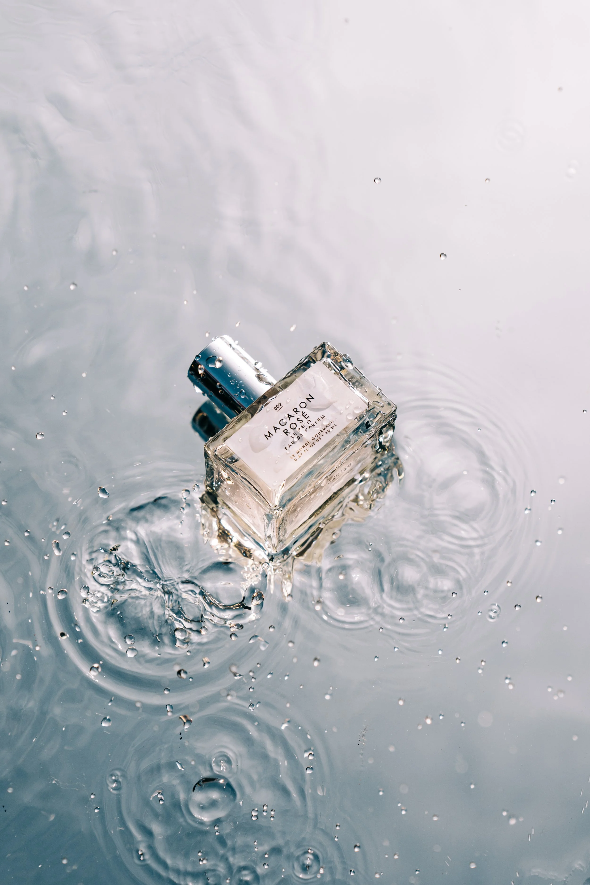 A bottle of Macarón perfume floating in water with ripples and water droplets.