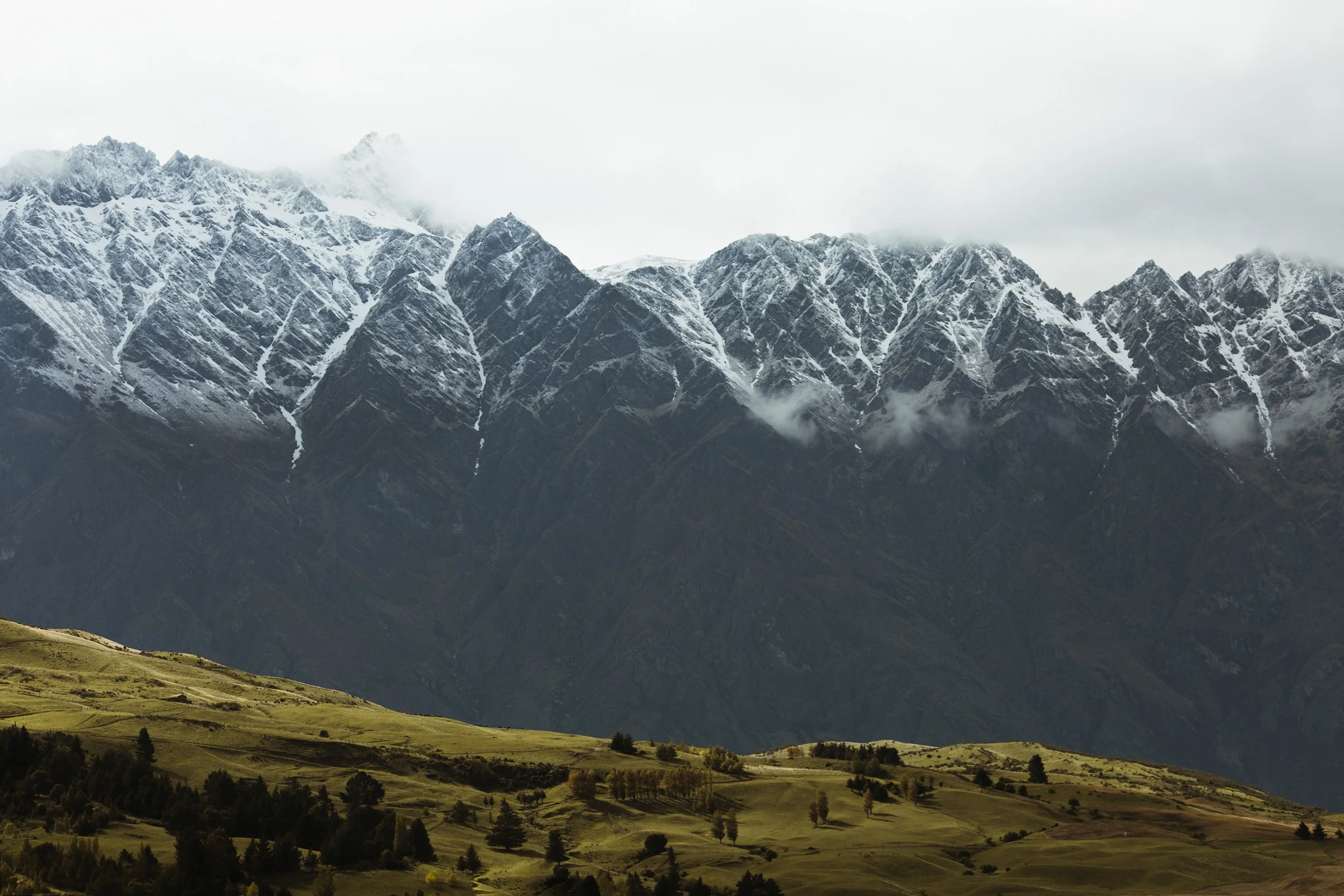 Mountain range with snow-capped peaks and lush green hills in the foreground