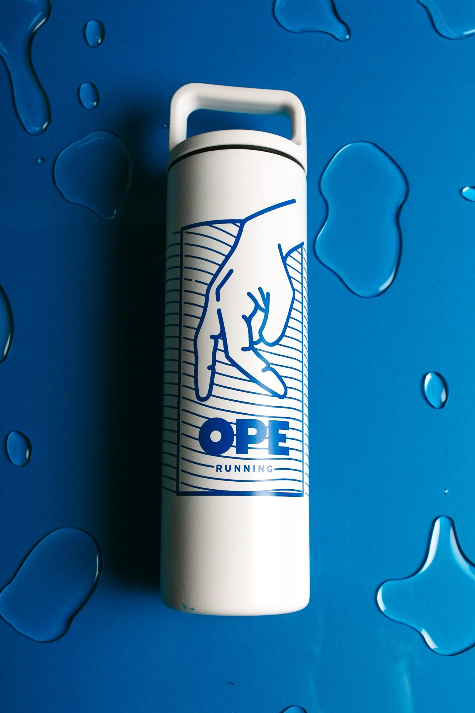 A white water bottle with a blue graphic of a hand making a pinching gesture and the words 'OPEN RUNNING' on it, placed on a blue background with water droplet patterns.