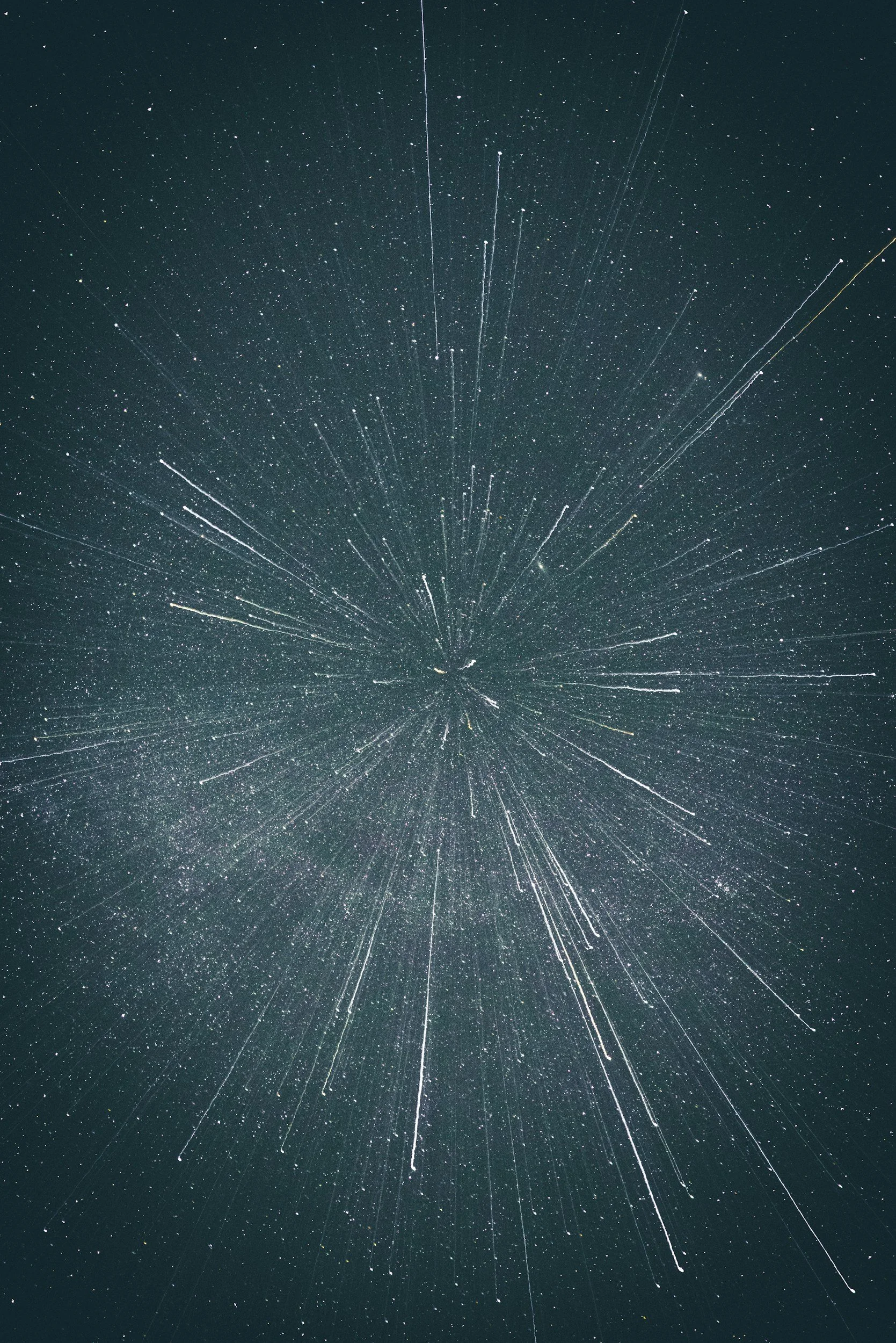 Long exposure photograph of the night sky capturing star trails radiating outward from the center.