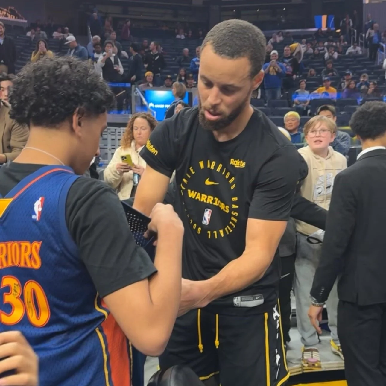 Stephen Curry of the Golden State Warriors signing an autograph for a young fan at a basketball game.