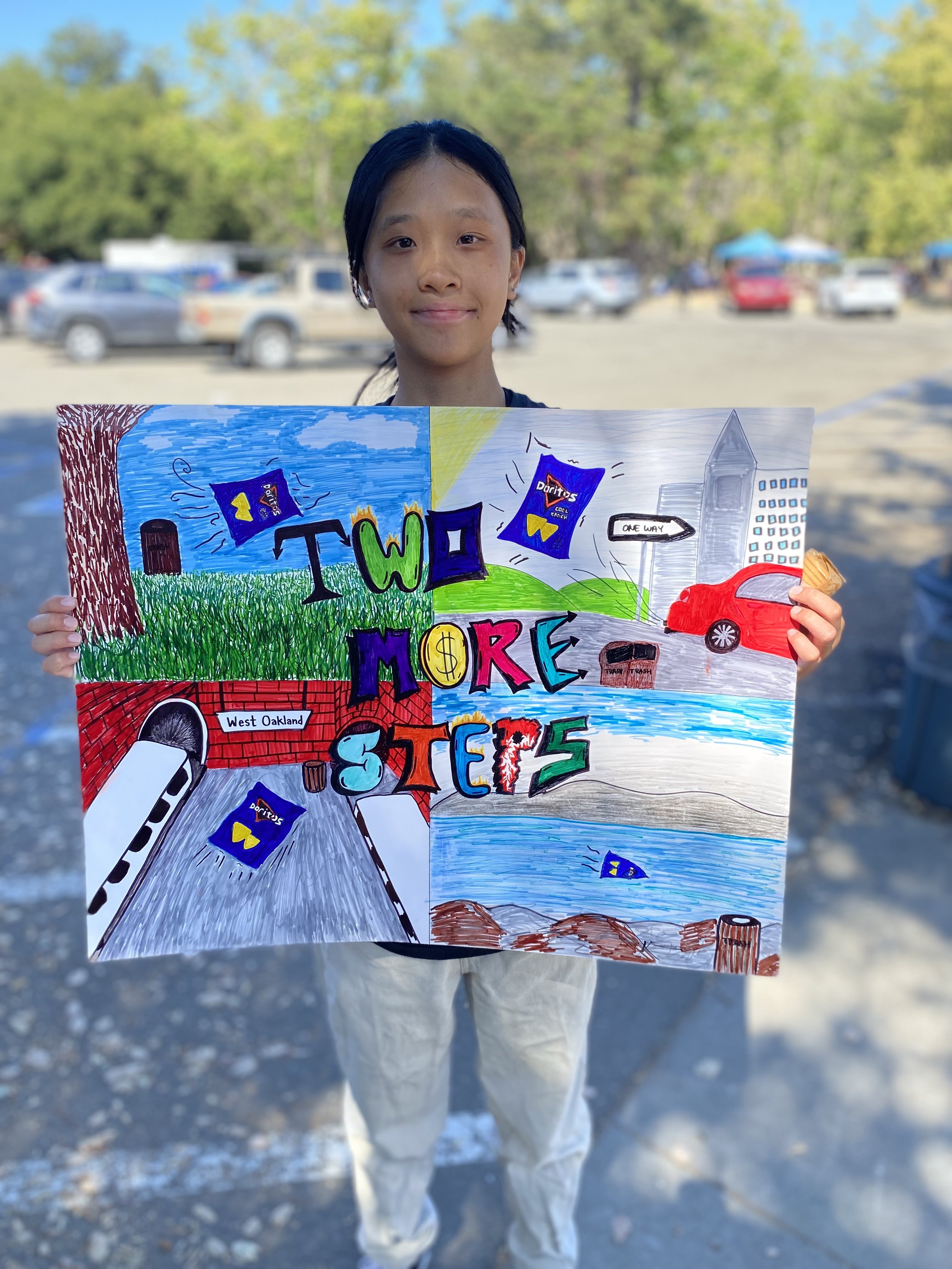 Young girl holding colorful protest sign outdoors with trees and parking lot in the background.