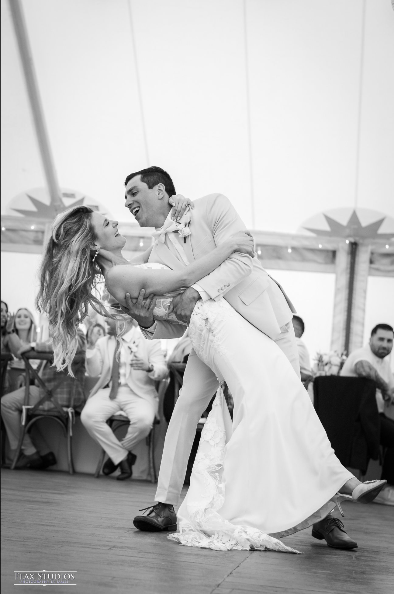 A bride and groom dancing at their wedding reception, with wedding guests watching in the background.