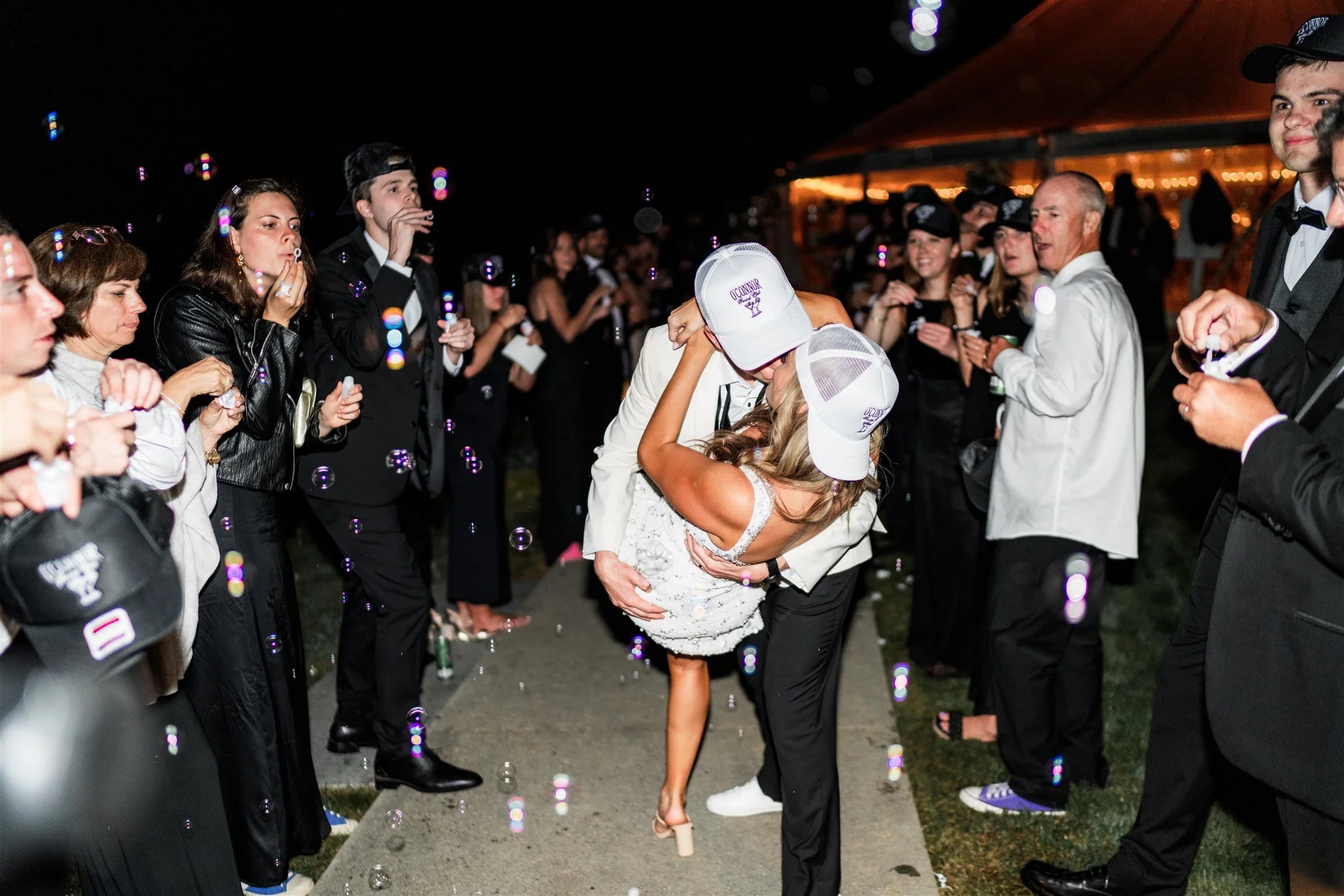 A bride and groom kissing and dancing in the middle of a crowd of wedding guests at night, with bubbles floating around.