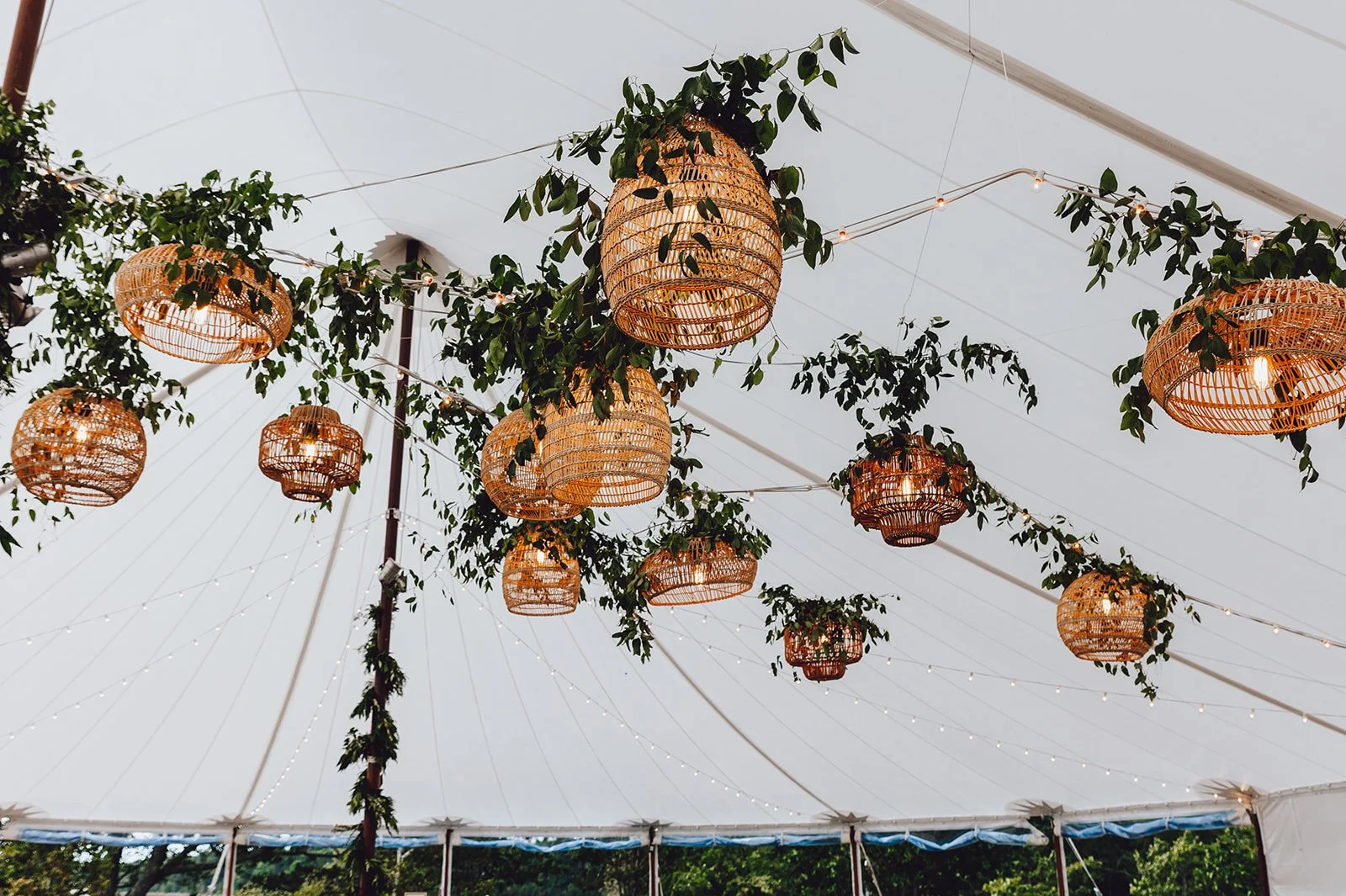 Decorative hanging lanterns and draped greenery under a large tent ceiling with string lights.