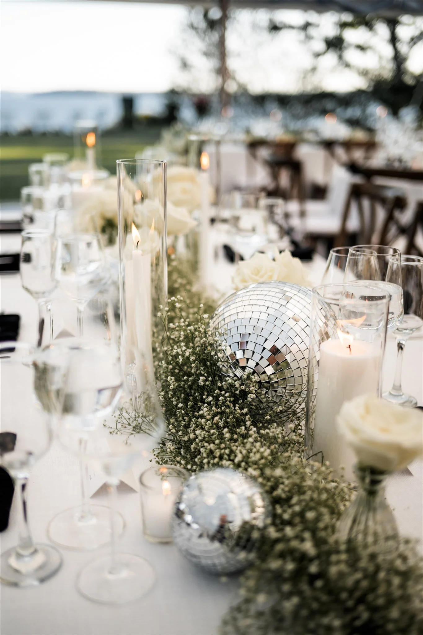 Elegant outdoor wedding reception table with white roses, candles, and disco ball decorations.
