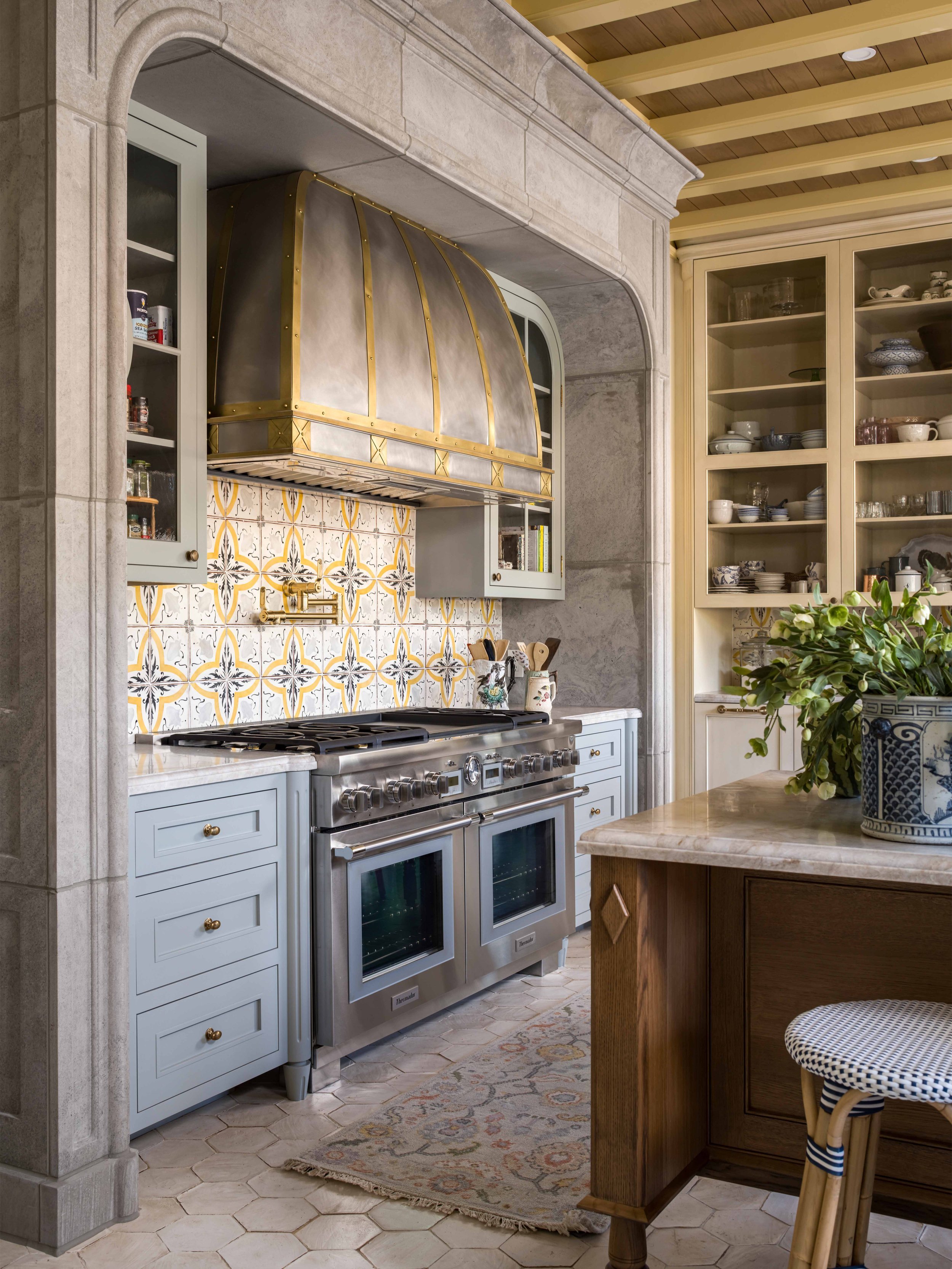 Kitchen with a large, stainless steel stove, a patterned backsplash, light-colored cabinetry, and a wooden island with a plant on it.