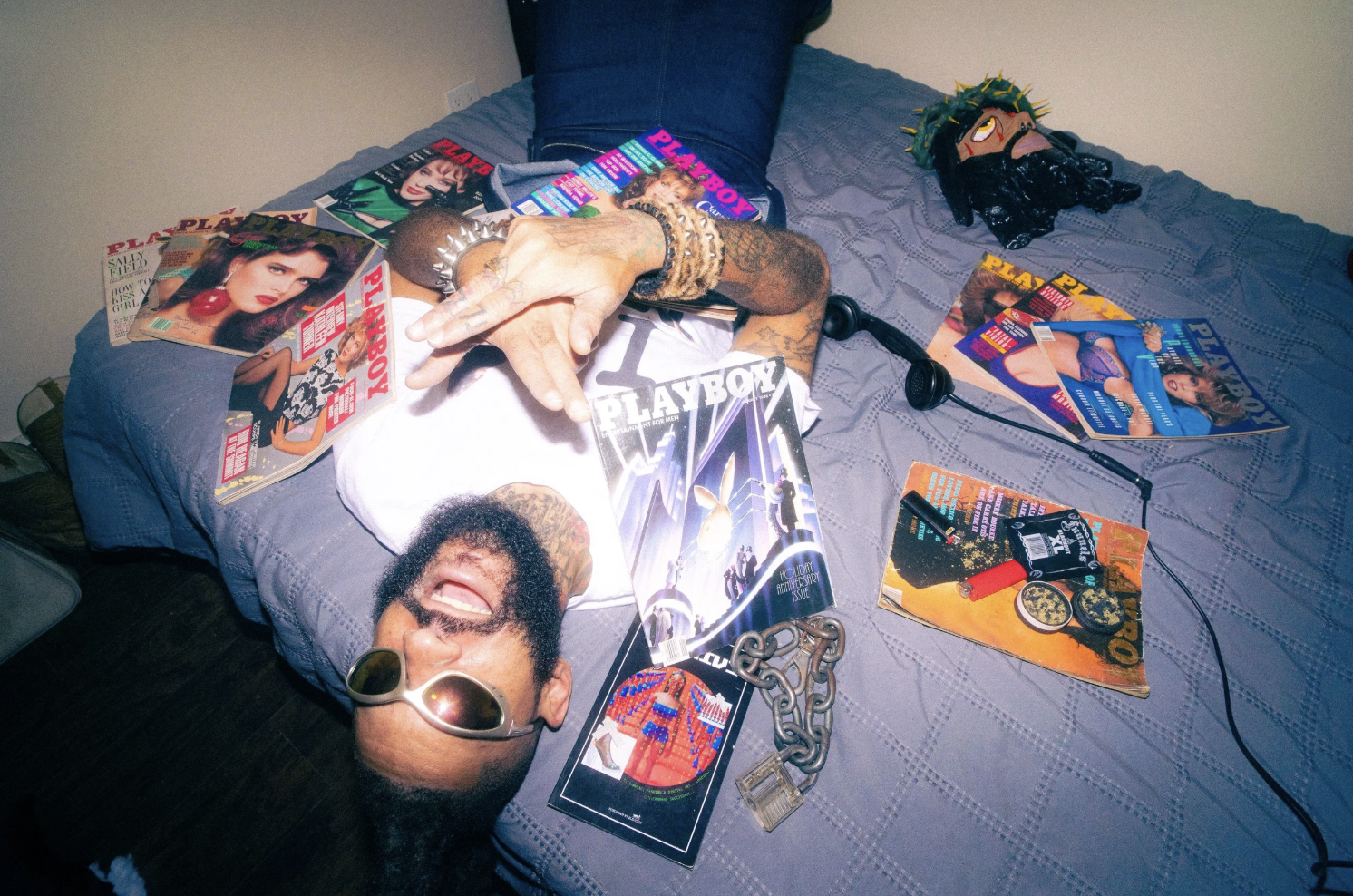 Music artist YONDER laying in bed with magazines spread over his body