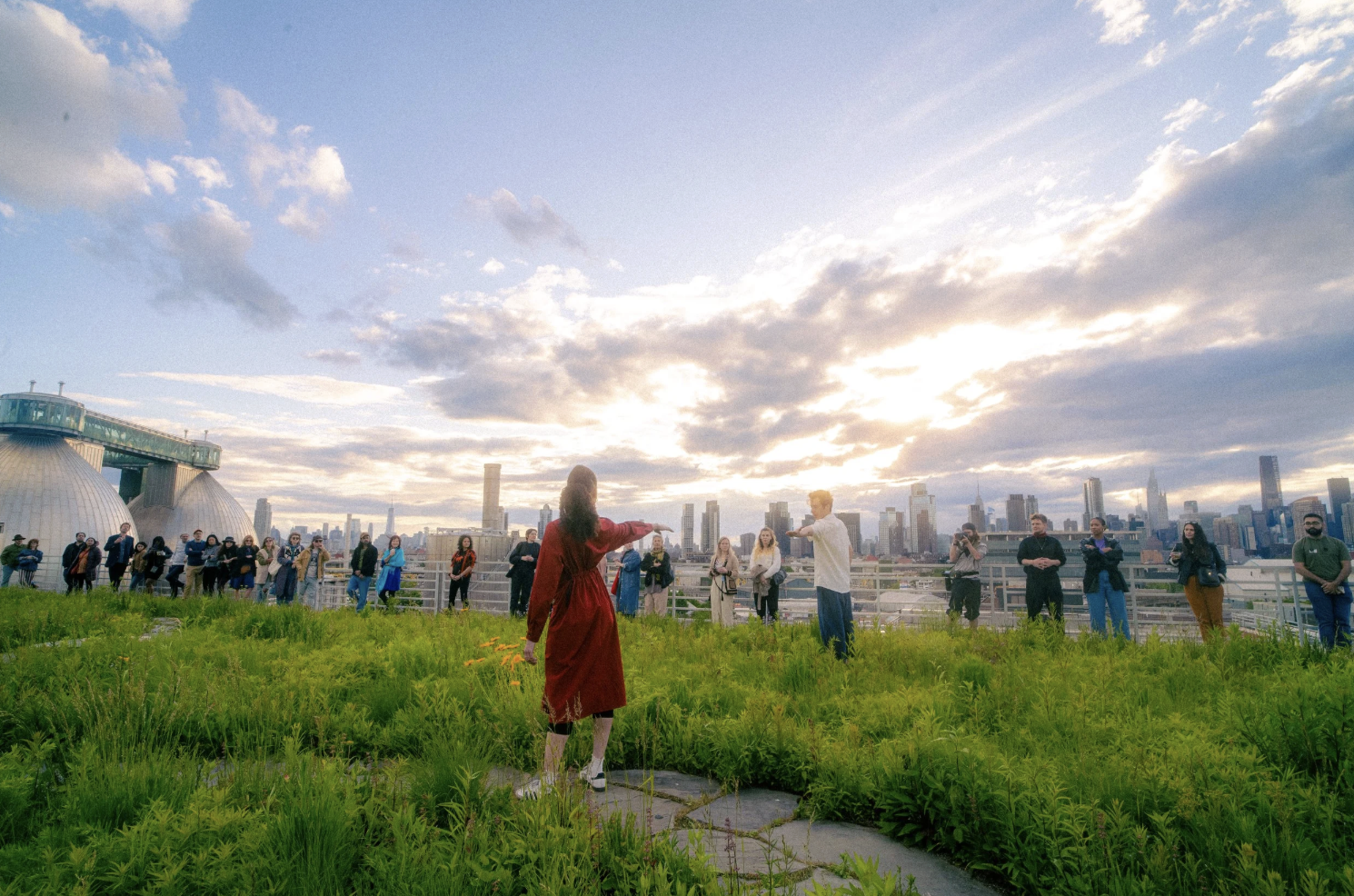 People participating in a wedding ceremony on a rooftop, with a city skyline and a sunset sky in the background.