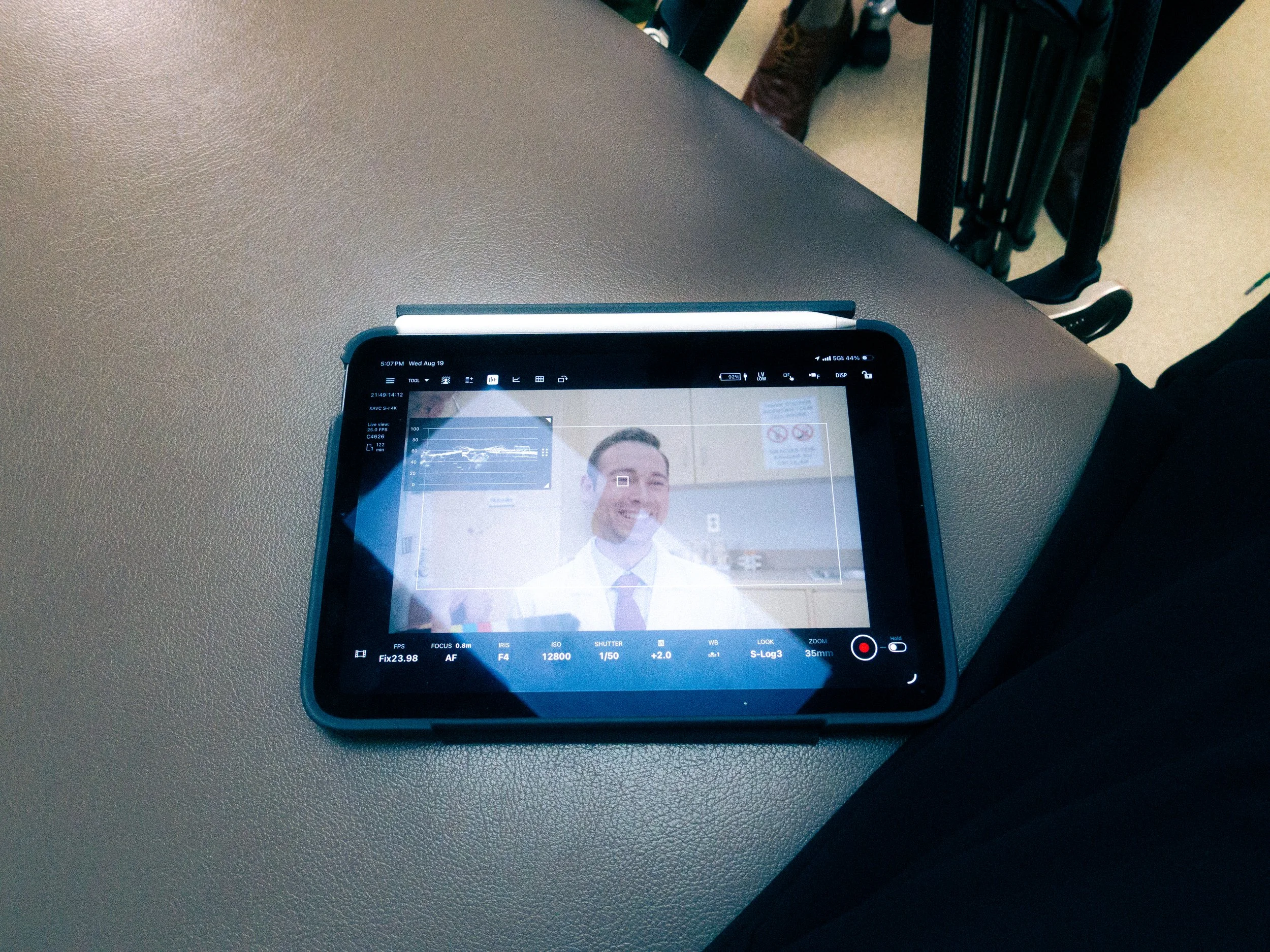 A tablet displaying a smiling man in a white shirt and tie, used for video recording or photo capturing.