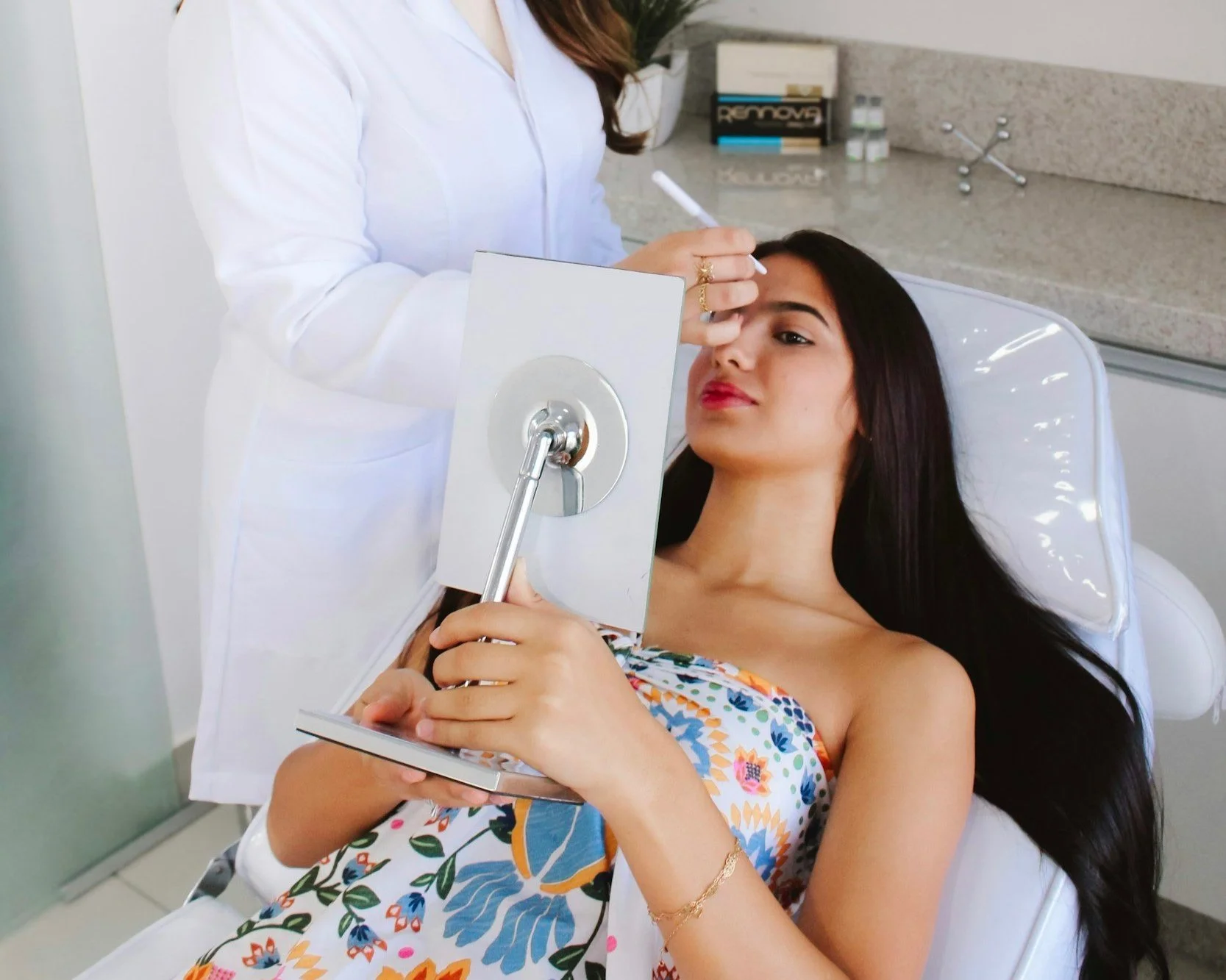 A woman with long dark hair lying on a dental chair, receiving consultation from a healthcare professional in a clinical setting.