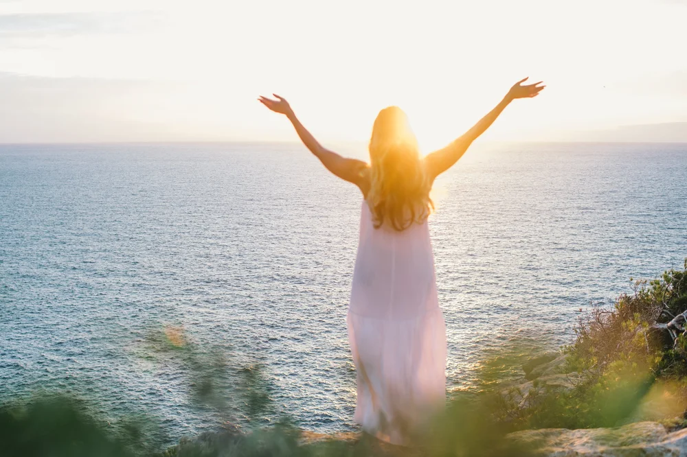 A woman with arms raised to the sea
