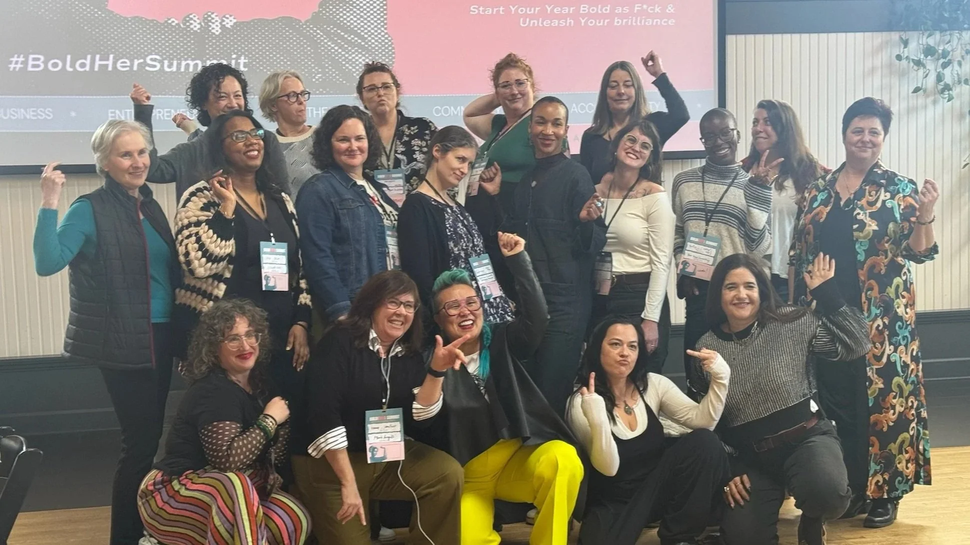 A group of women in three rows cheering and making strong arms and funny faces.