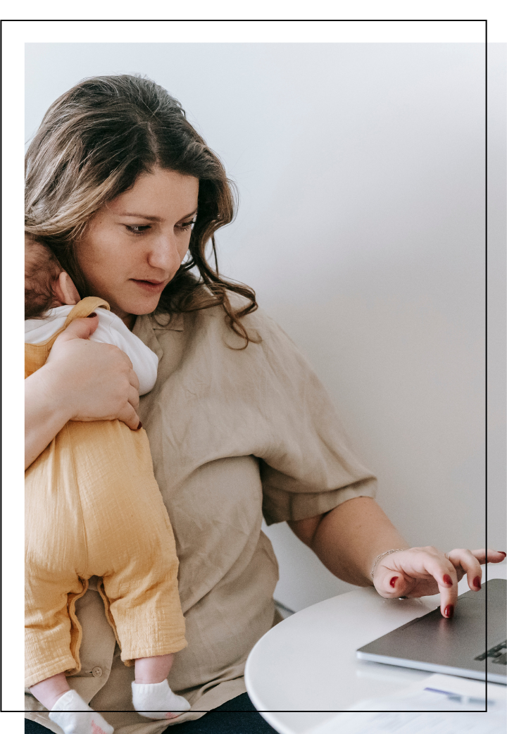 A woman holding a small child on her lap while sitting at a white table using a laptop.