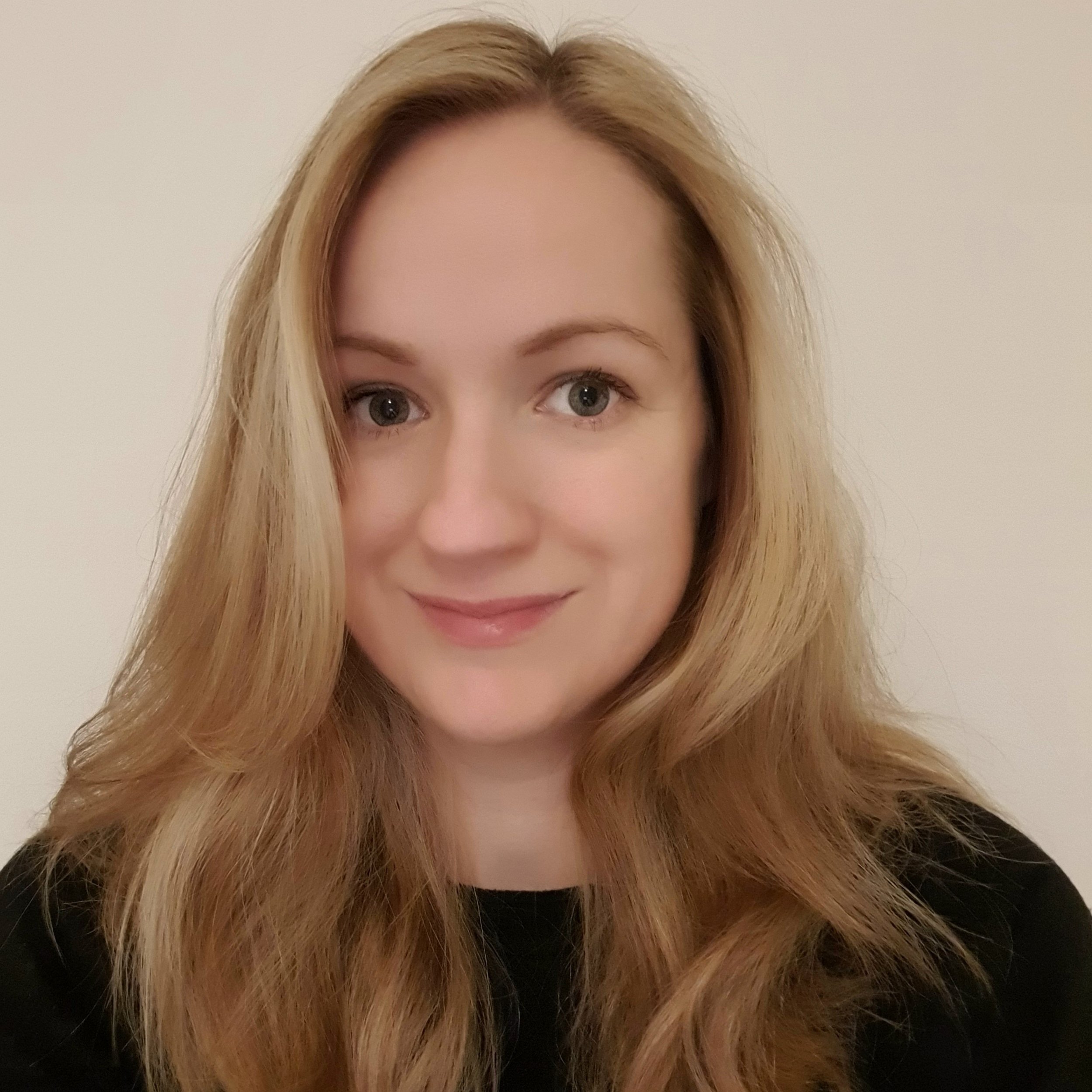A close-up photo of a woman with long, wavy, blonde hair, fair skin, and blue eyes, smiling slightly, wearing a black top, standing against a plain white background. Photo of Sarah Miller Financial Adviser