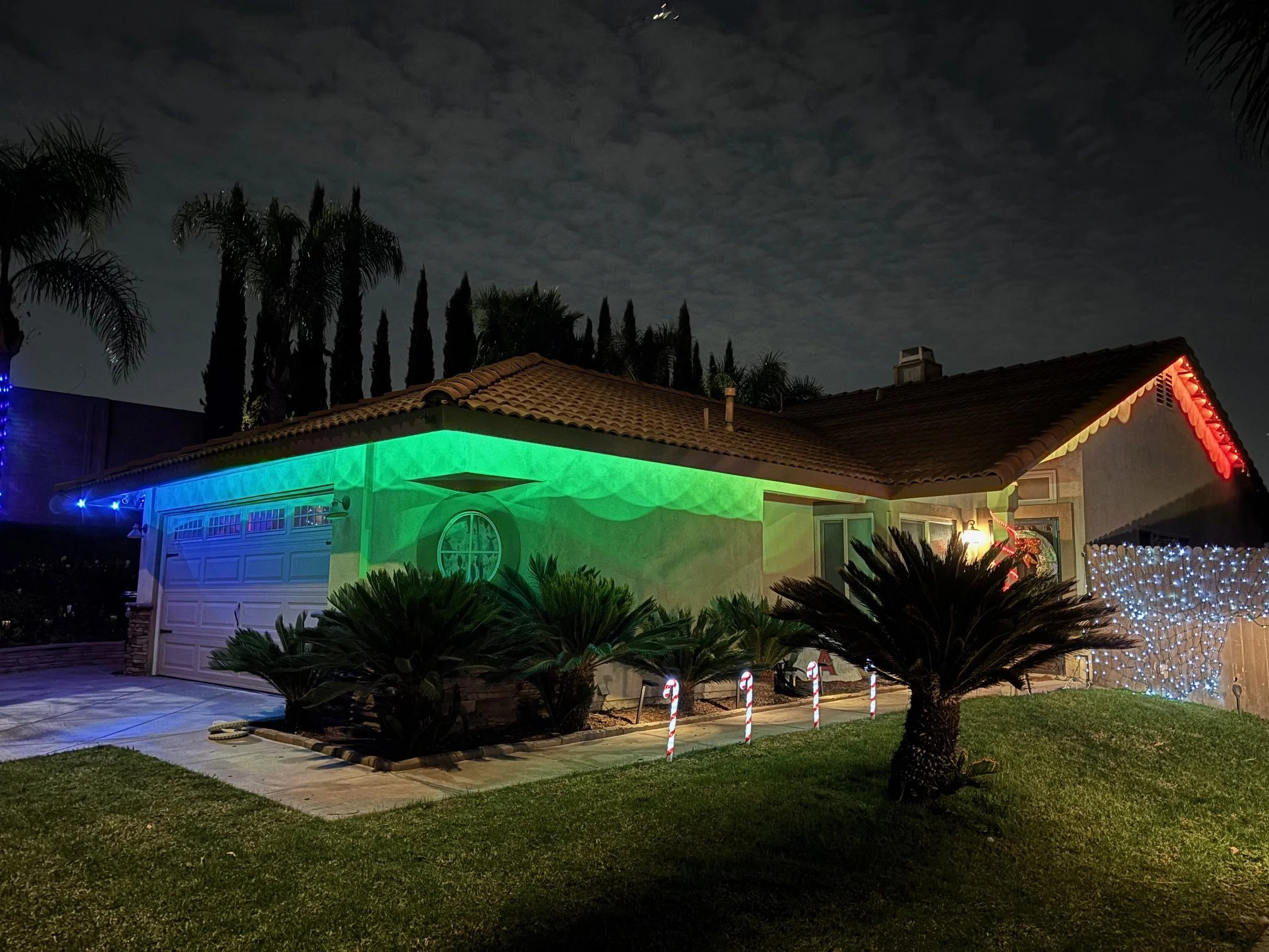 A house decorated with colorful Christmas lights at night, showing green, red, and white lighting on the exterior.