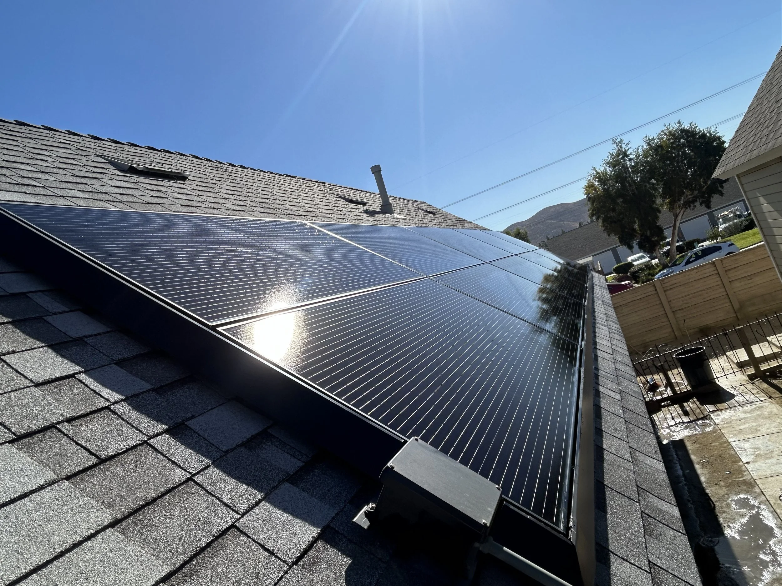 Solar panels installed on a house roof reflecting sunlight with a clear blue sky in the background.