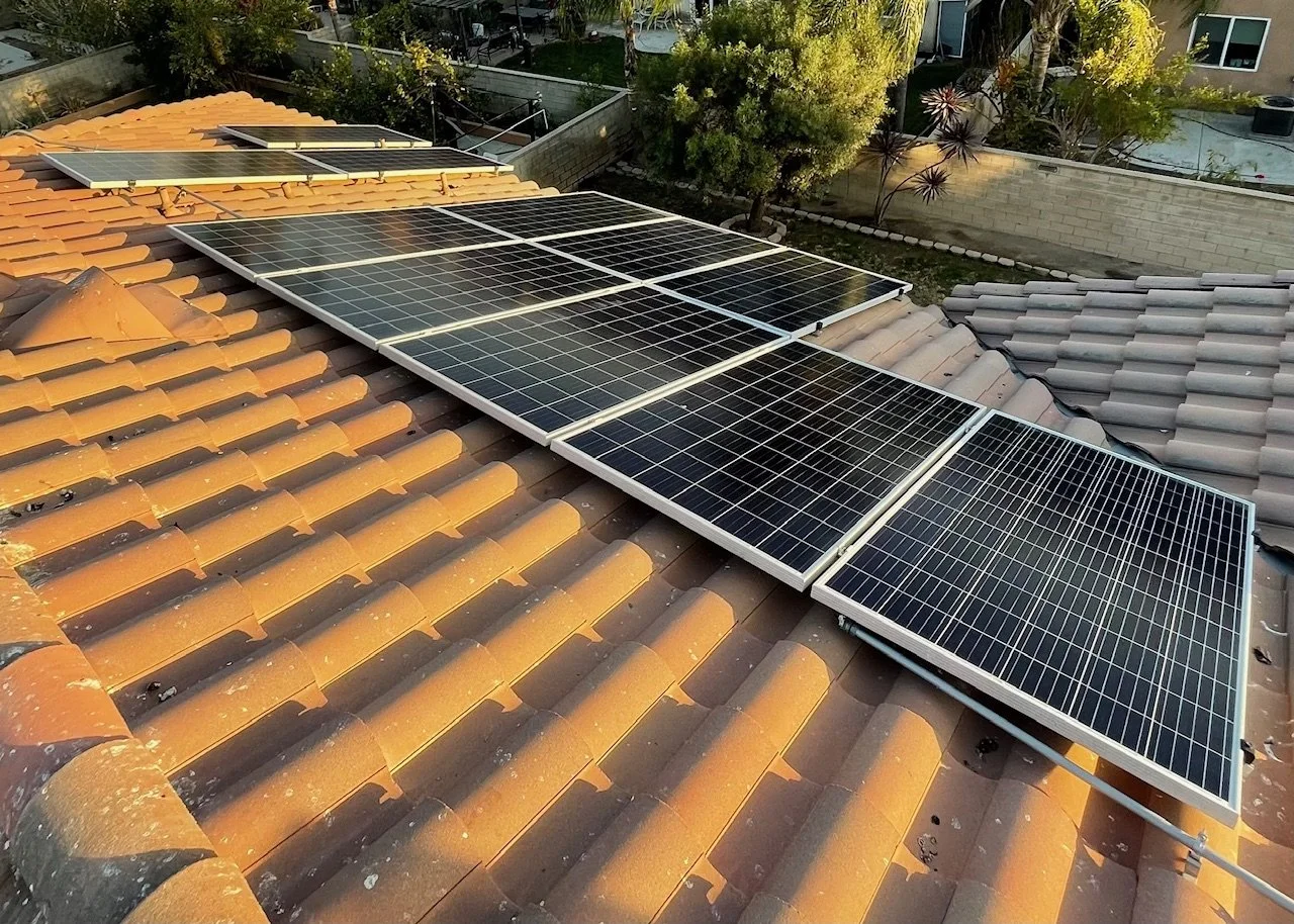 Solar panels installed on a tiled rooftop with trees and neighboring houses in the background.
