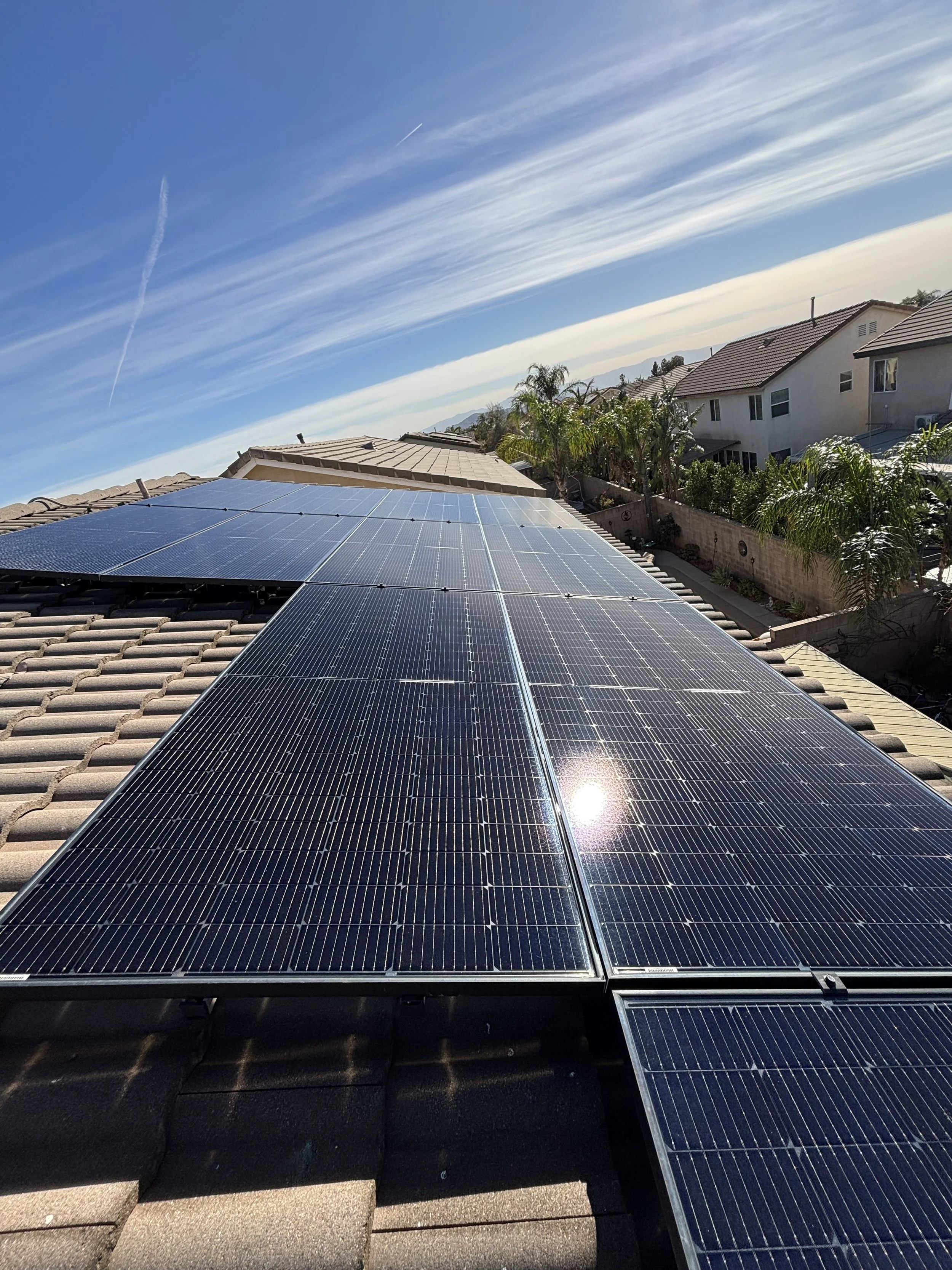 Solar panels installed on a residential roof under a blue sky with wispy clouds.