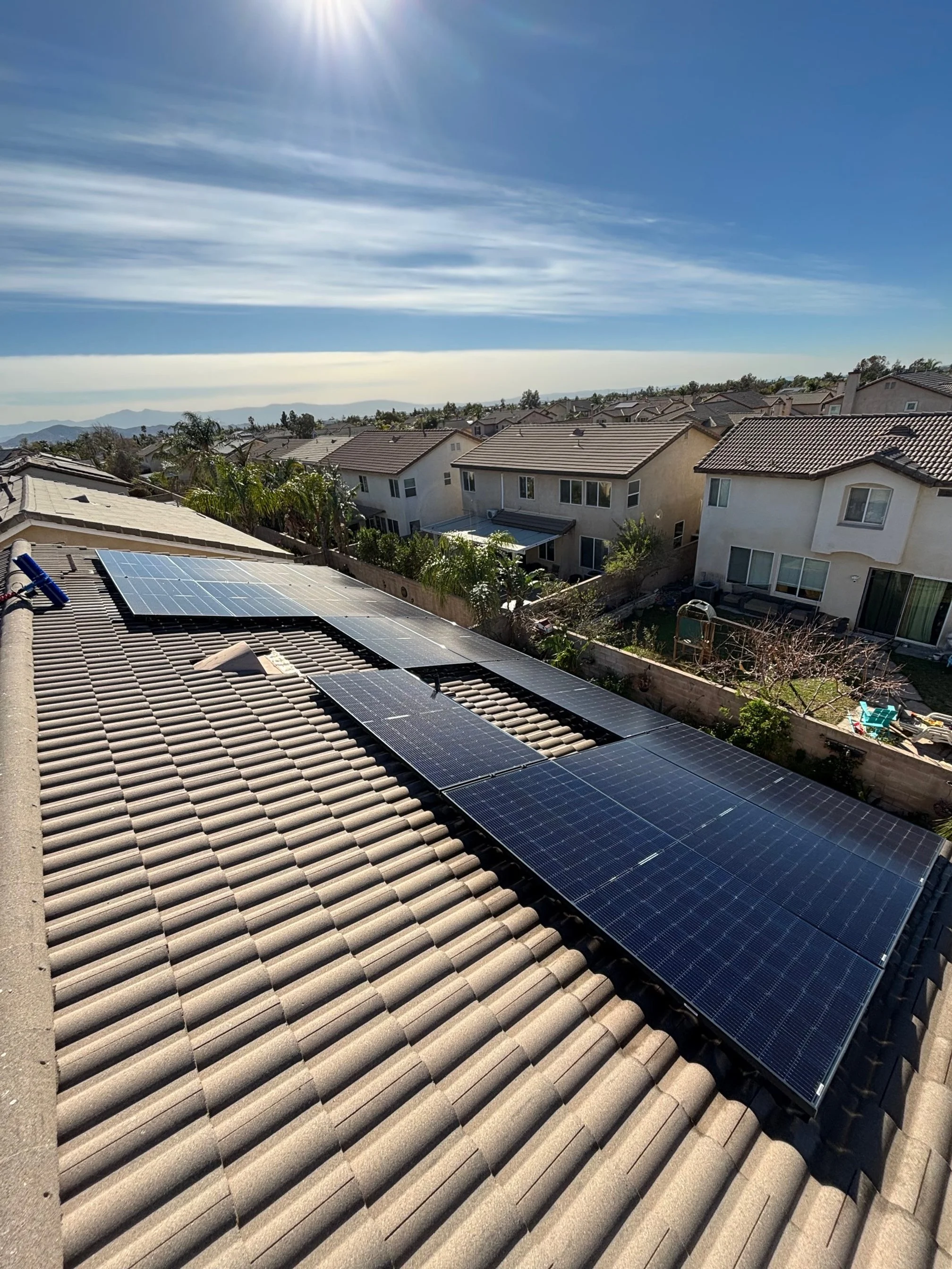 View of a residential neighborhood with solar panels installed on the tiled roof of a house under a sunny sky.