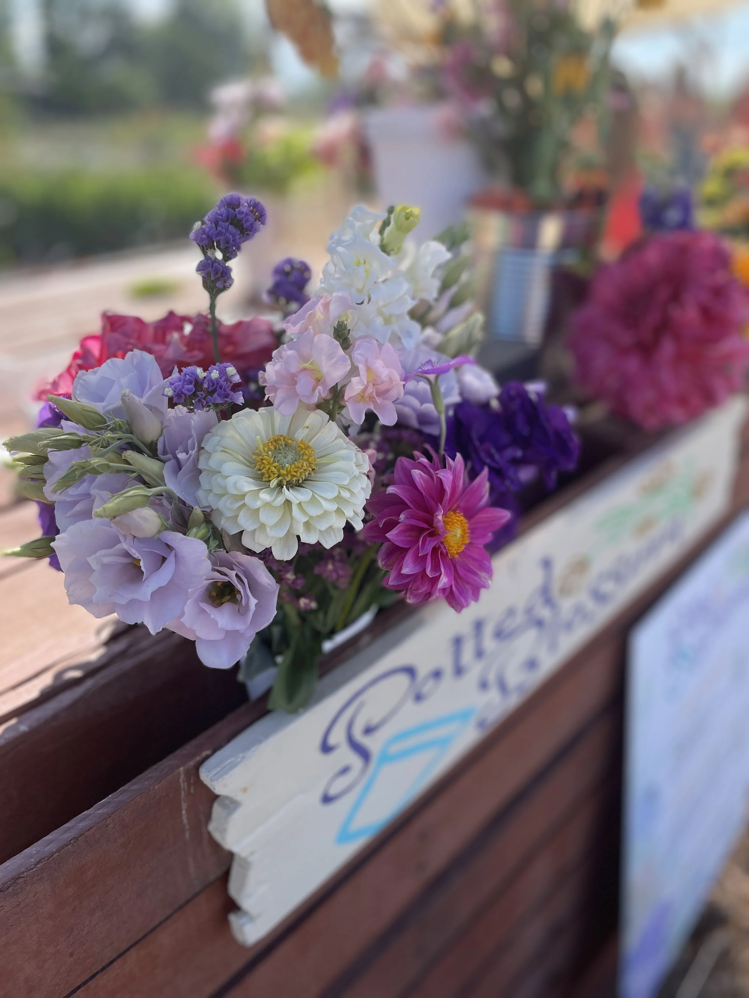 A colorful bouquet of flowers including purple, white, pink, and red blossoms displayed on a wooden surface at an outdoor market or garden.