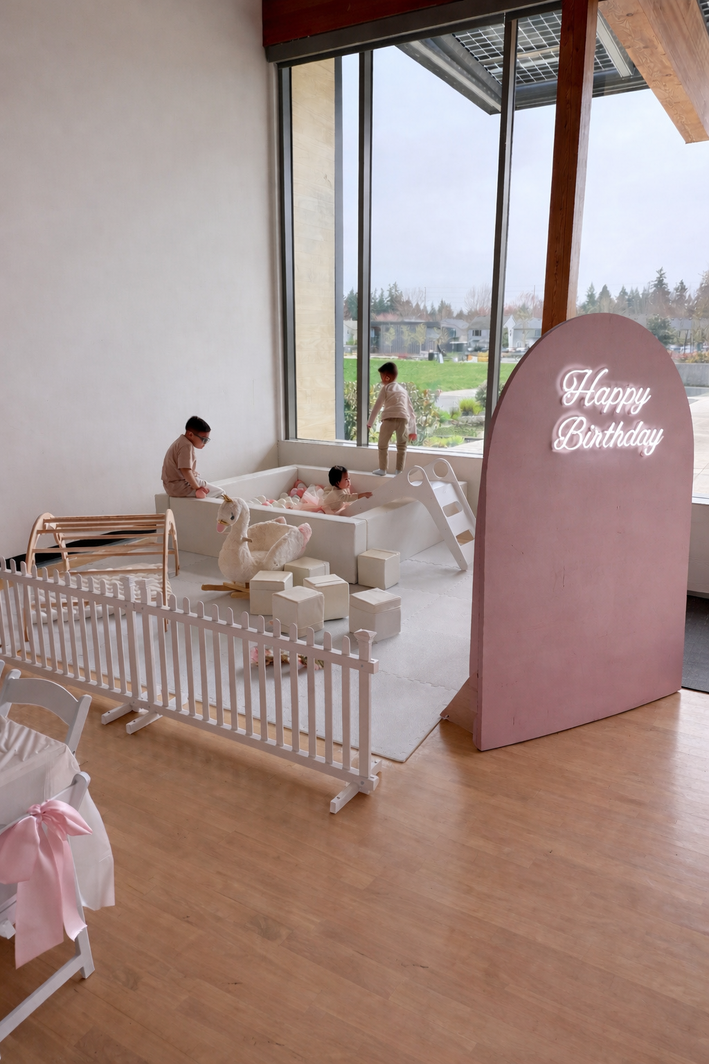 Children playing in a pastel pink and white birthday party area with a plush unicorn and a "Happy Birthday" sign.