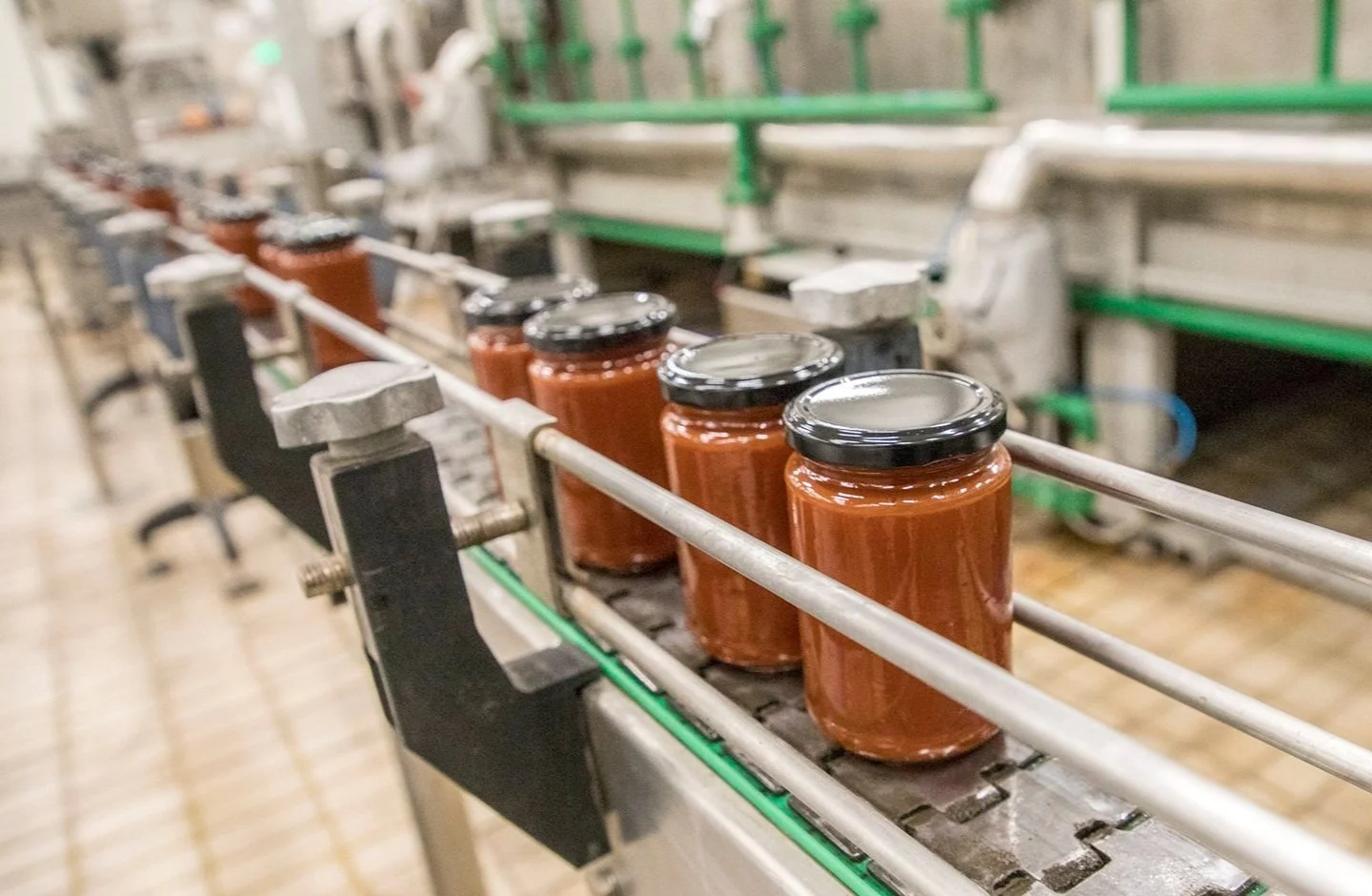 Jars of tomato sauce on a conveyor belt in a food processing facility.