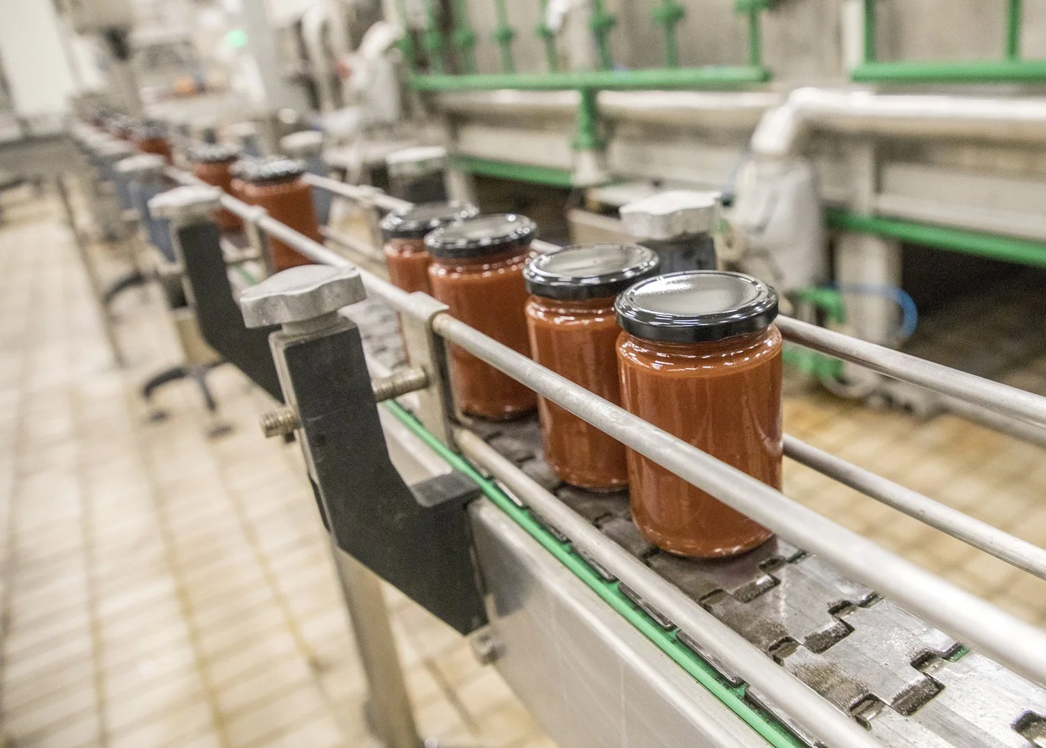Jars of tomato sauce moving along an industrial conveyor belt in a factory setting.