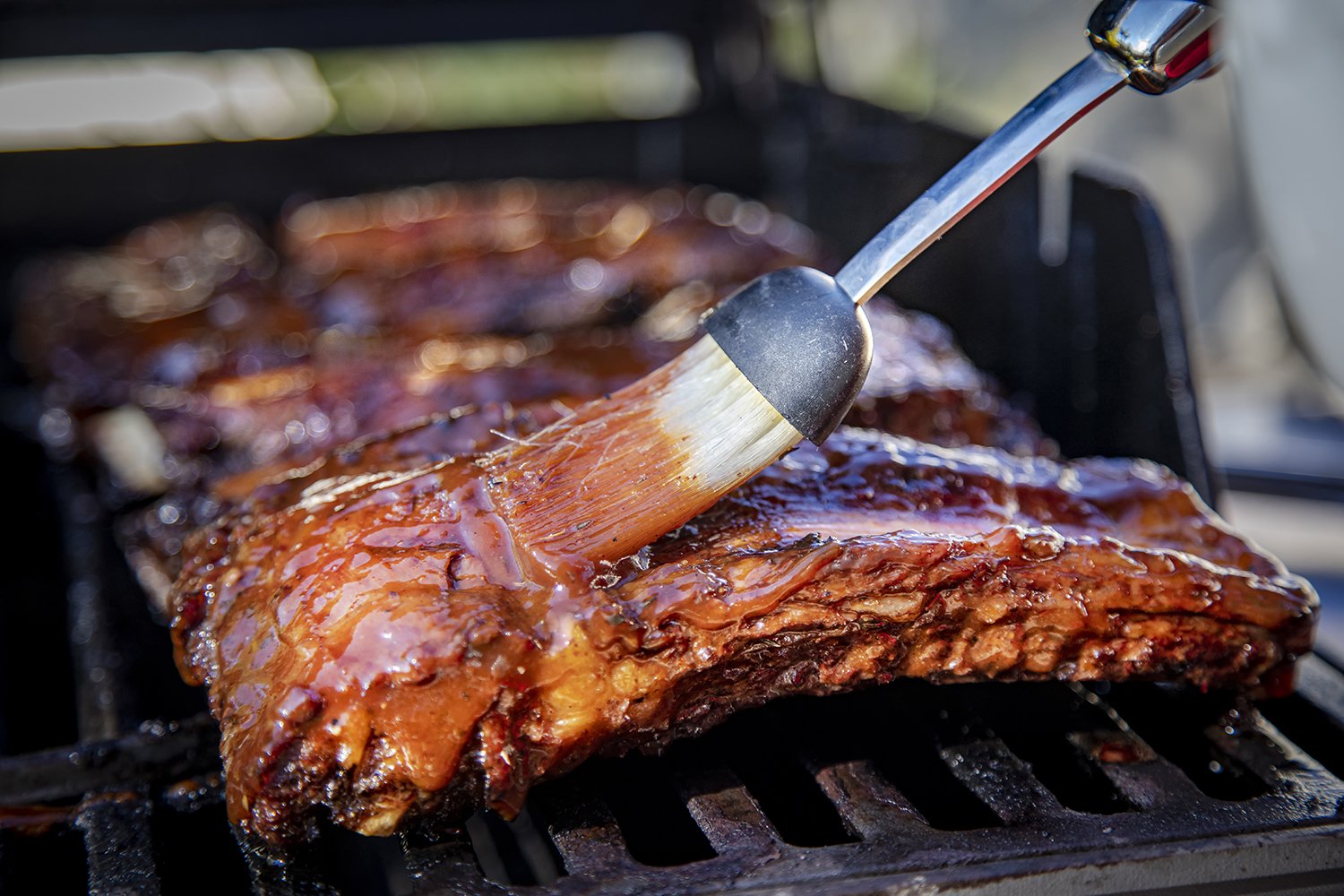 Barbecue ribs being glazed with sauce on a grill.