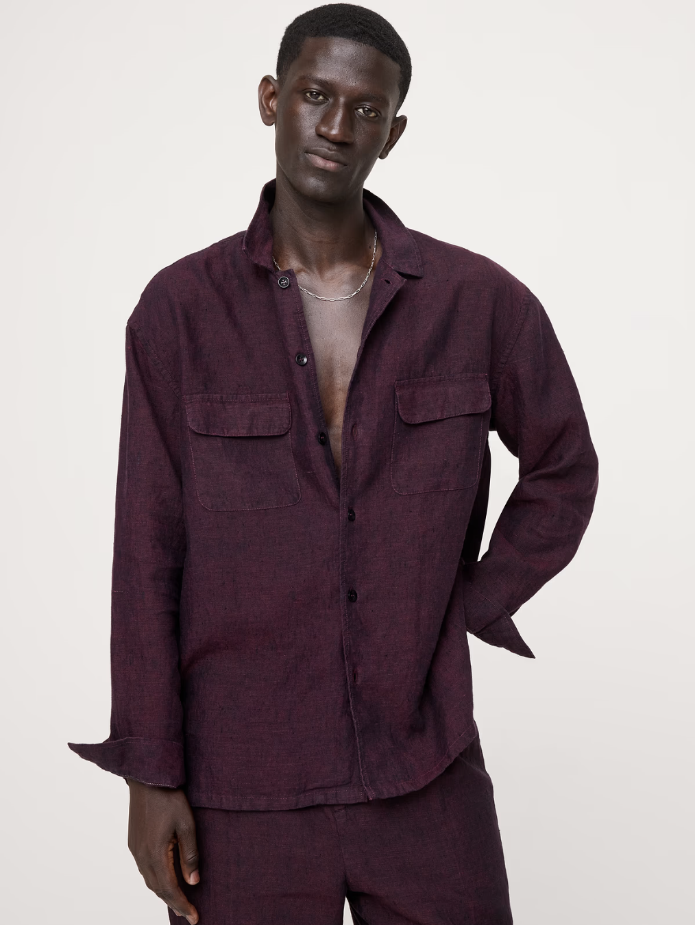 A close-up shot of a man wearing a Banana Republic Relaxed-Fit linen long-sleeve shirt in a deep plum purple, featuring dual chest utility pockets.