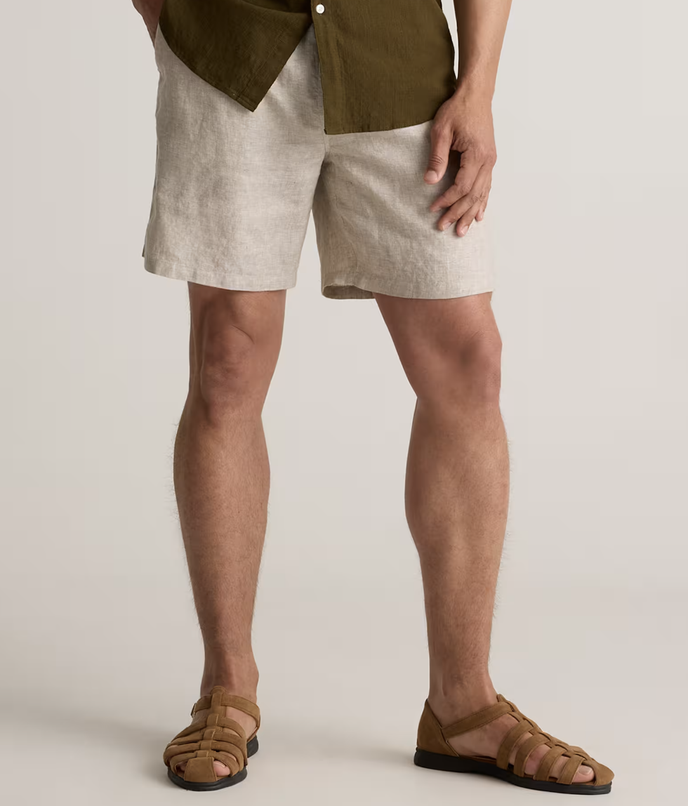 A man wearing light beige 100% European linen drawstring shorts from Quince paired with brown leather fisherman sandals.