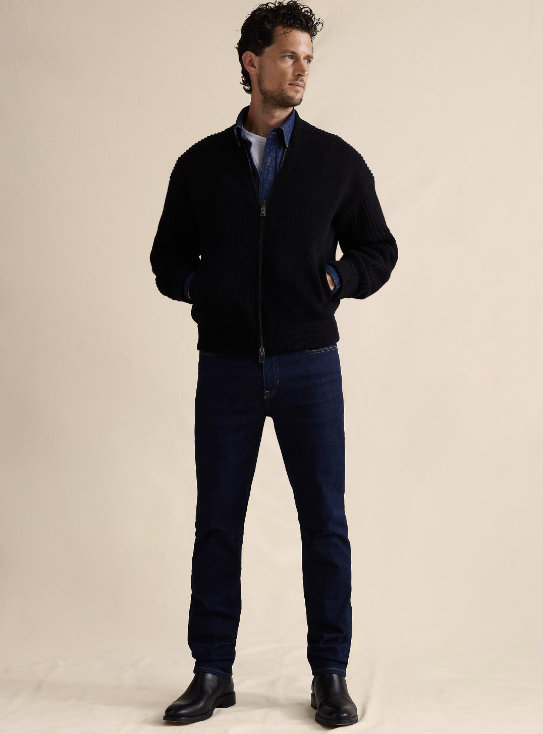 Man wearing a navy blue Naked Cashmere Phillip quarter-zip sweater over a denim shirt with dark jeans.