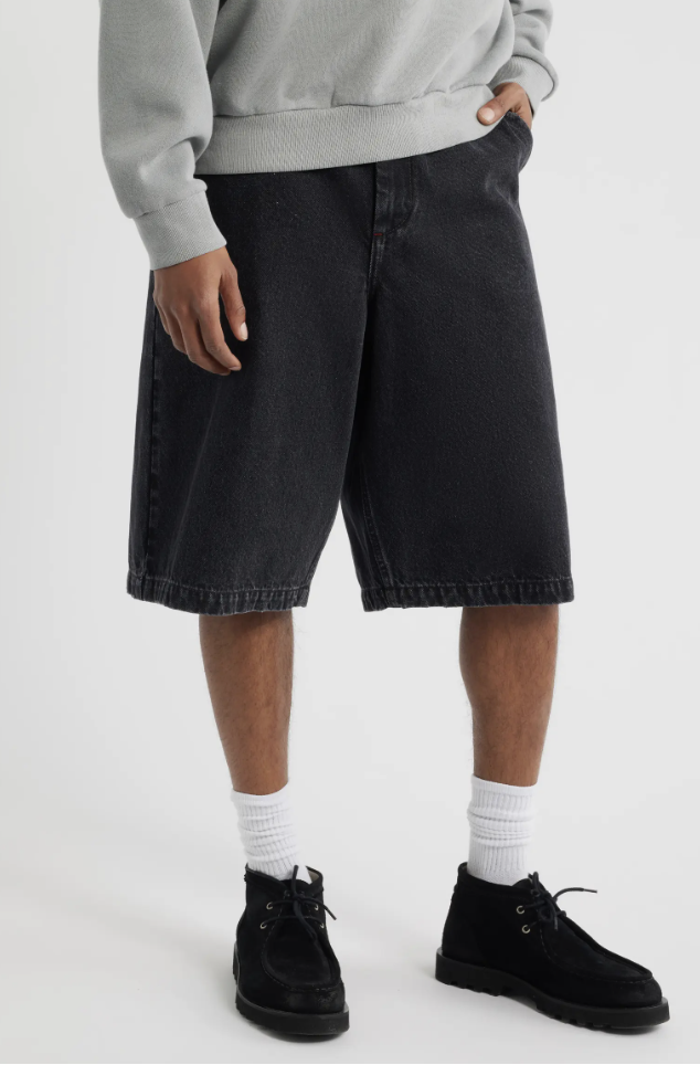 A man wearing oversized black denim shorts from Elwood, styled with white crew socks and black suede desert boots for a modern streetwear look.