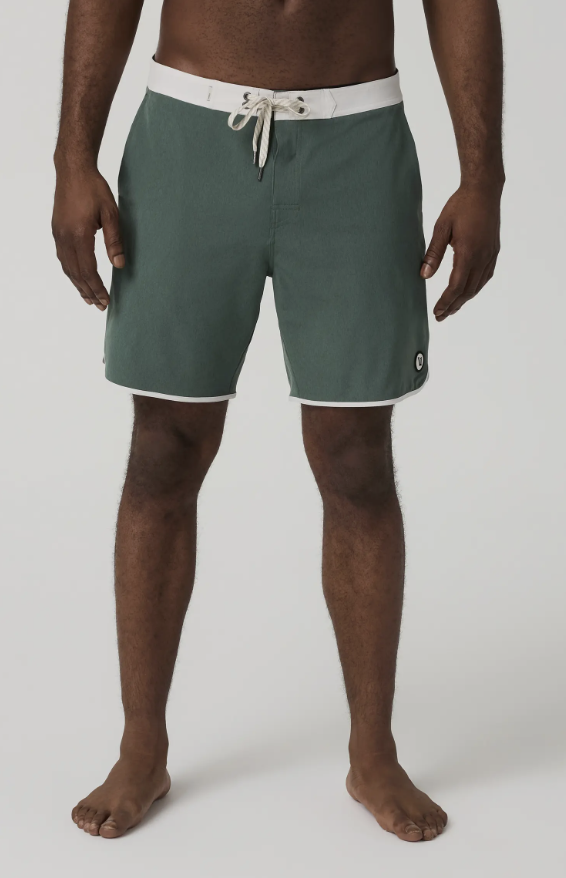 A man wearing dark sage green tailored swim trunks with a white drawstring, designed to look like casual shorts for the 2026 summer season.