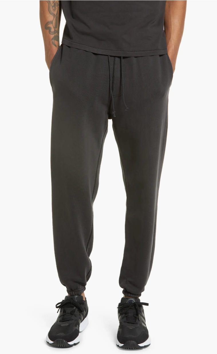 Man wearing black Elwood organic cotton brushed terry sweatpants with black New Balance sneakers.