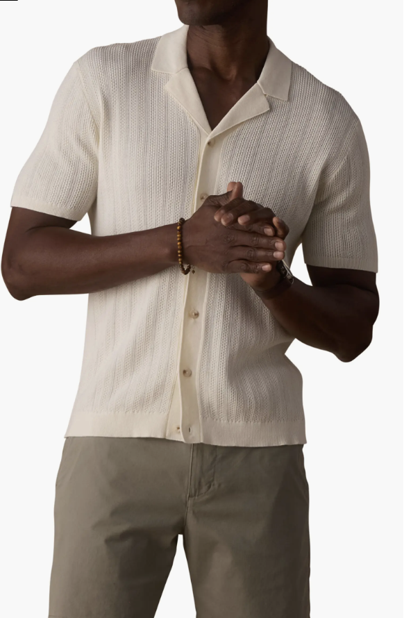 A man wearing a cream-colored lightweight knit polo shirt with a flat collar and button-down front, styled for a 2026 men's summer wardrobe.