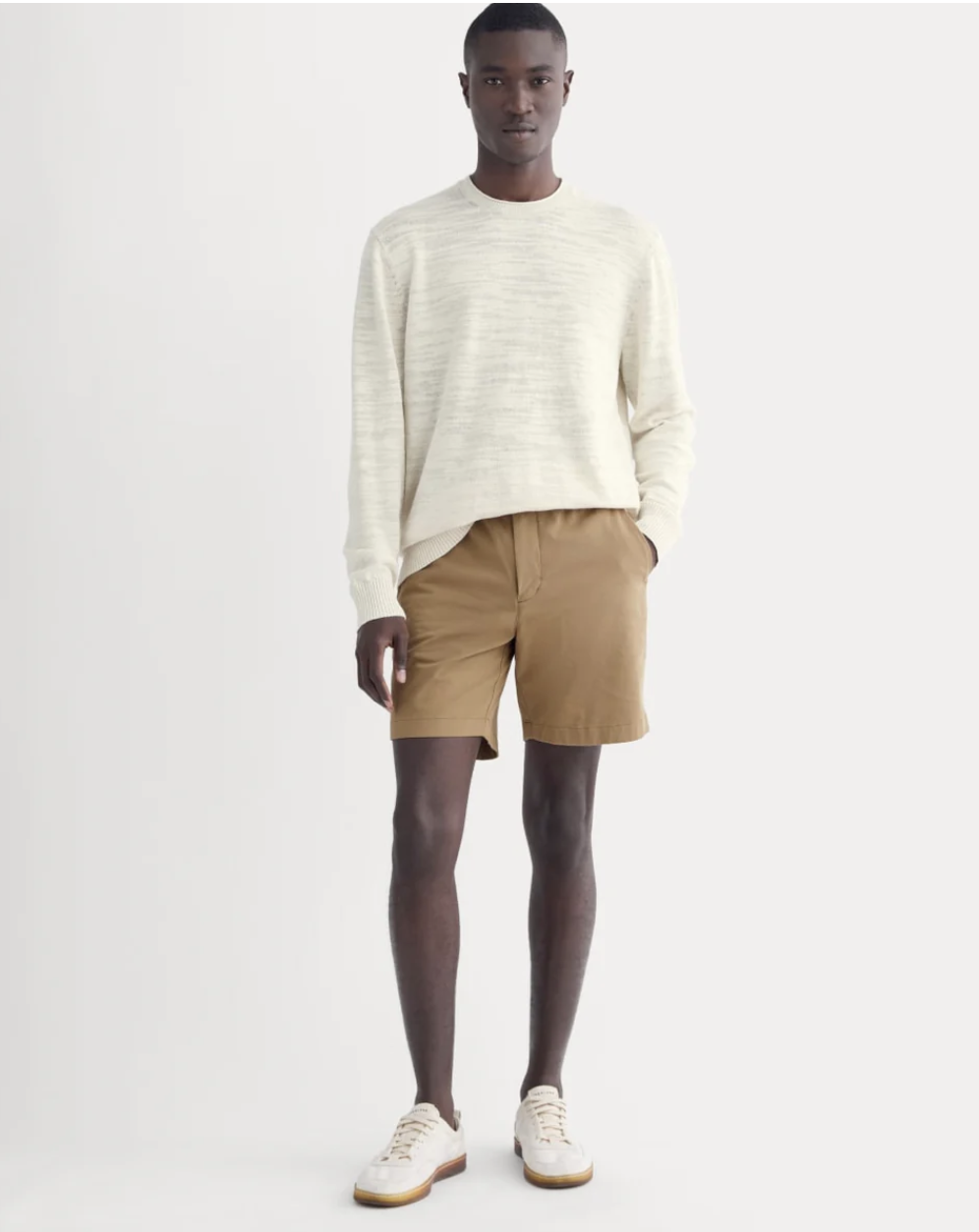 A man wearing khaki Everlane Pull-On Performance Chino shorts, styled with a cream textured long-sleeve shirt and white leather sneakers.