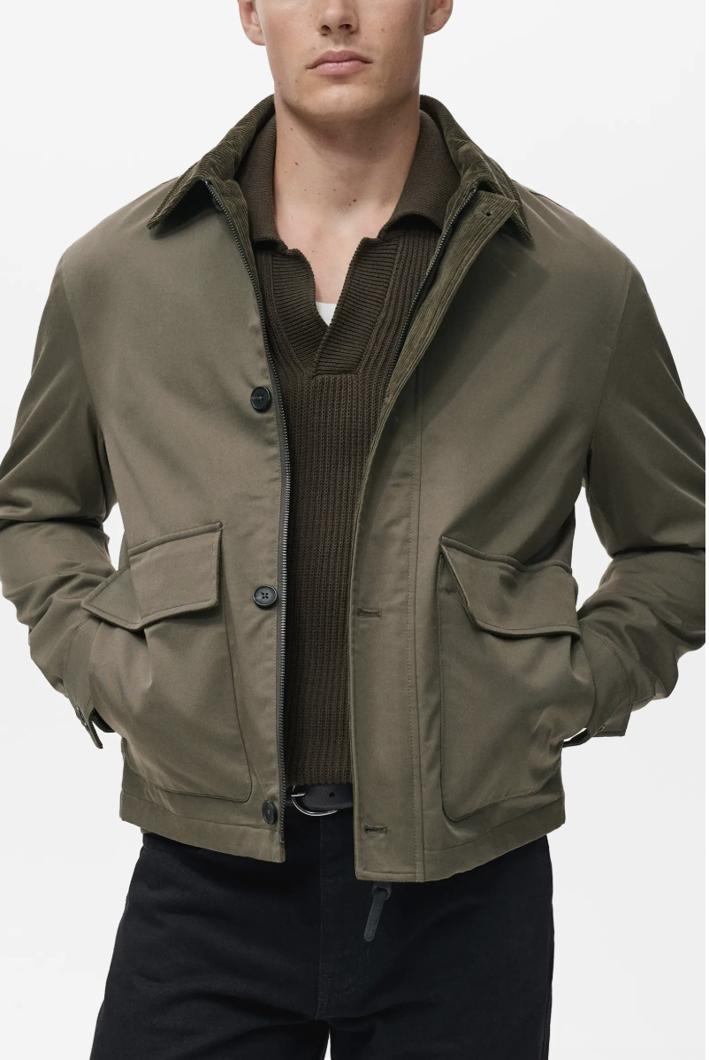 Man wearing an olive green water-repellent station jacket over a dark brown textured knit polo shirt.