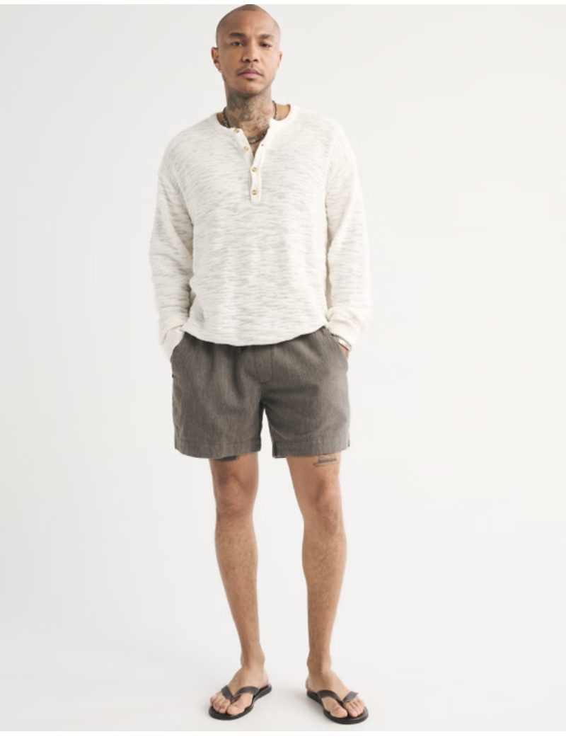 A man wearing grey Abercrombie linen-blend pull-on shorts with a 6-inch inseam, styled with black flip-flops and a white long-sleeve linen shirt.