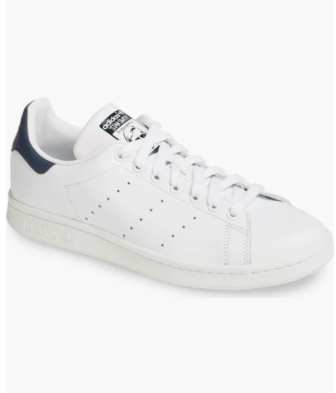 A side profile view of a classic white leather Adidas Stan Smith sneaker featuring a dark navy blue heel tab and perforated three-stripe details.
