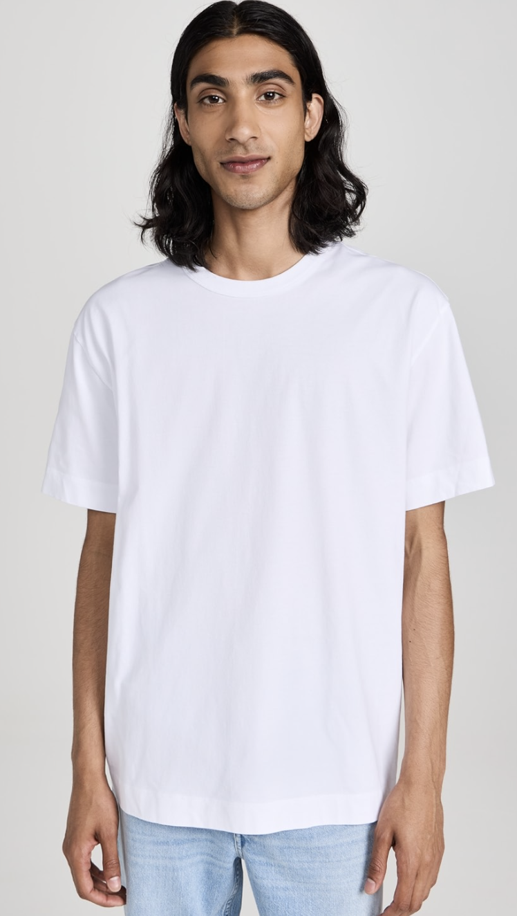 Close-up of a man wearing a crisp white crew neck t-shirt with a structured collar, tucked into dark navy trousers for a classic men's minimalist look.