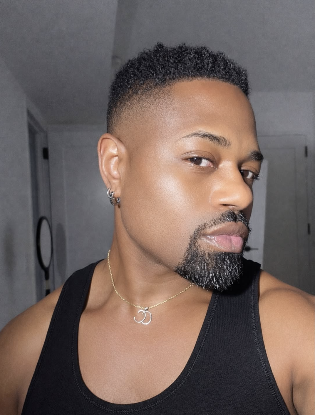 Close-up portrait of a man showcasing a sharply lined, modern goatee with a faded connection to a short mustache, a clean mid-skin fade haircut, and a gold chain necklace.
