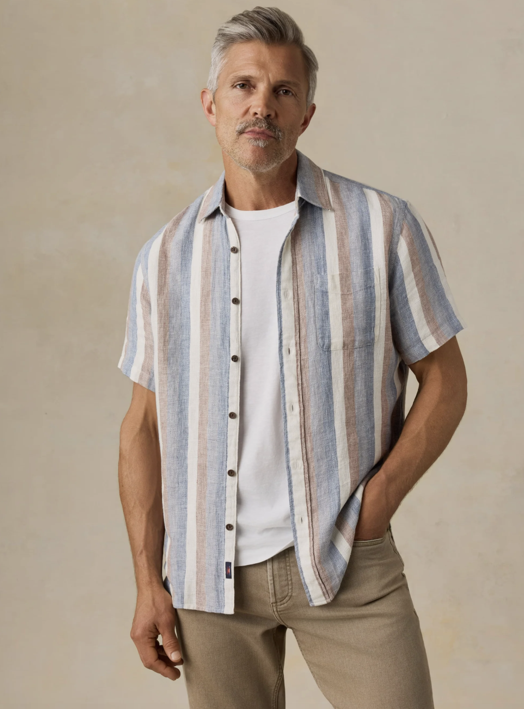 A front shot of a man wearing a Faherty short-sleeve linen shirt with vertical blue, beige, and white stripes, layered open over a classic white t-shirt.