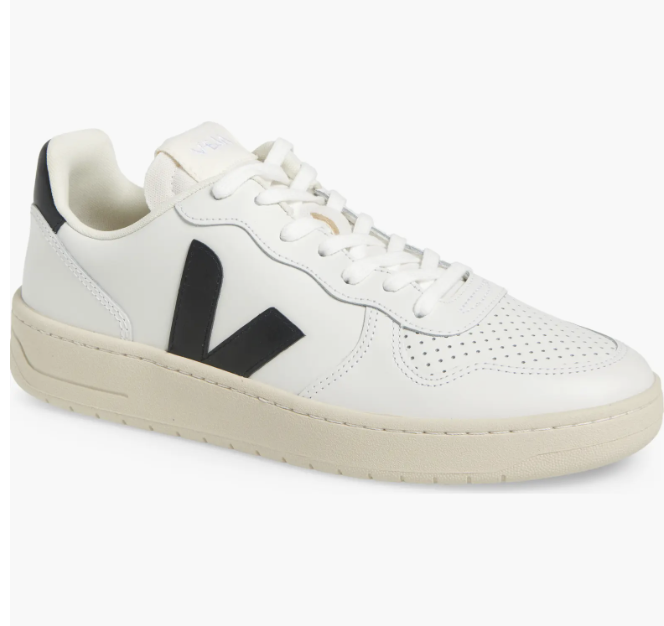 A side profile view of a white leather Veja V-10 sneaker featuring the brand's signature black 'V' logo, a perforated toe box, and an off-white rubber sole.